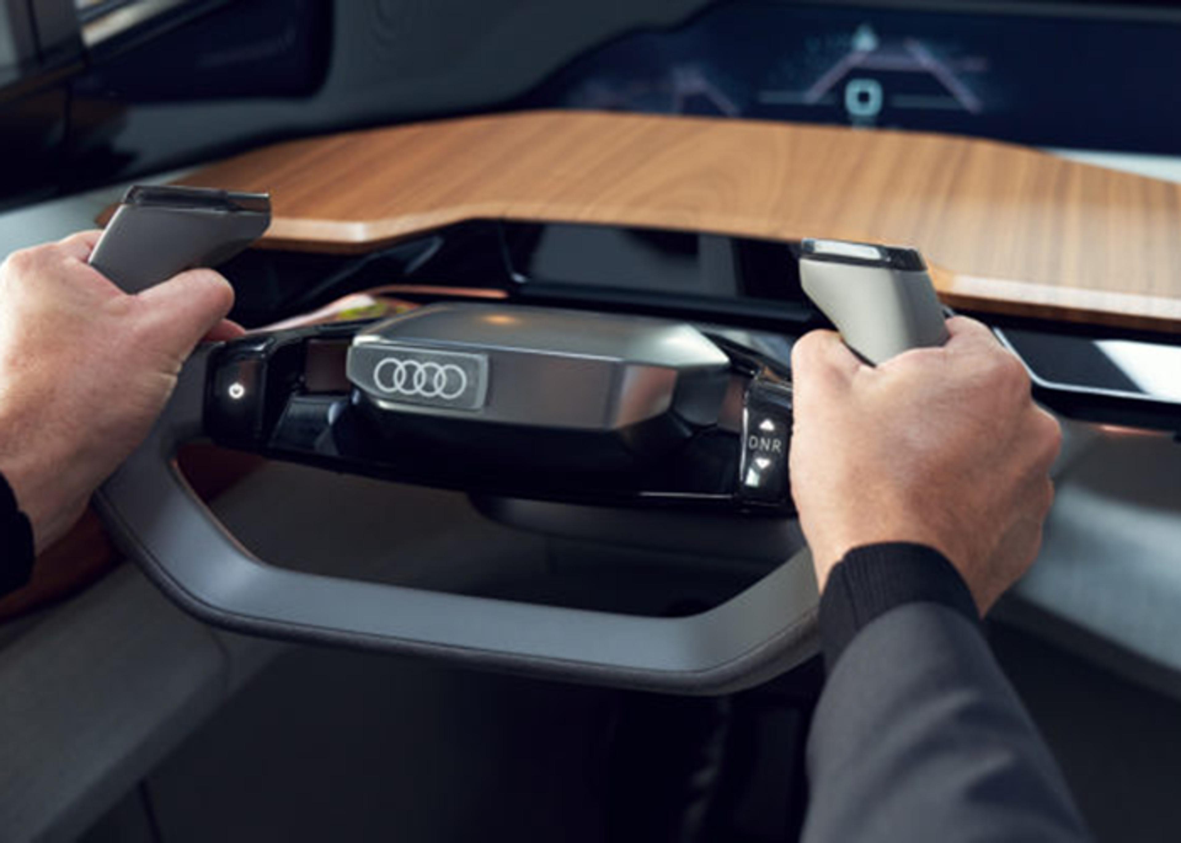 Interior view of the Audi Skysphere concept car, featuring a rectangular steering wheel with hand grips, an Audi emblem, and a wooden dashboard-like surface. A hand controls switches labeled "DNR" on the steering wheel. A digital display is visible in the background.