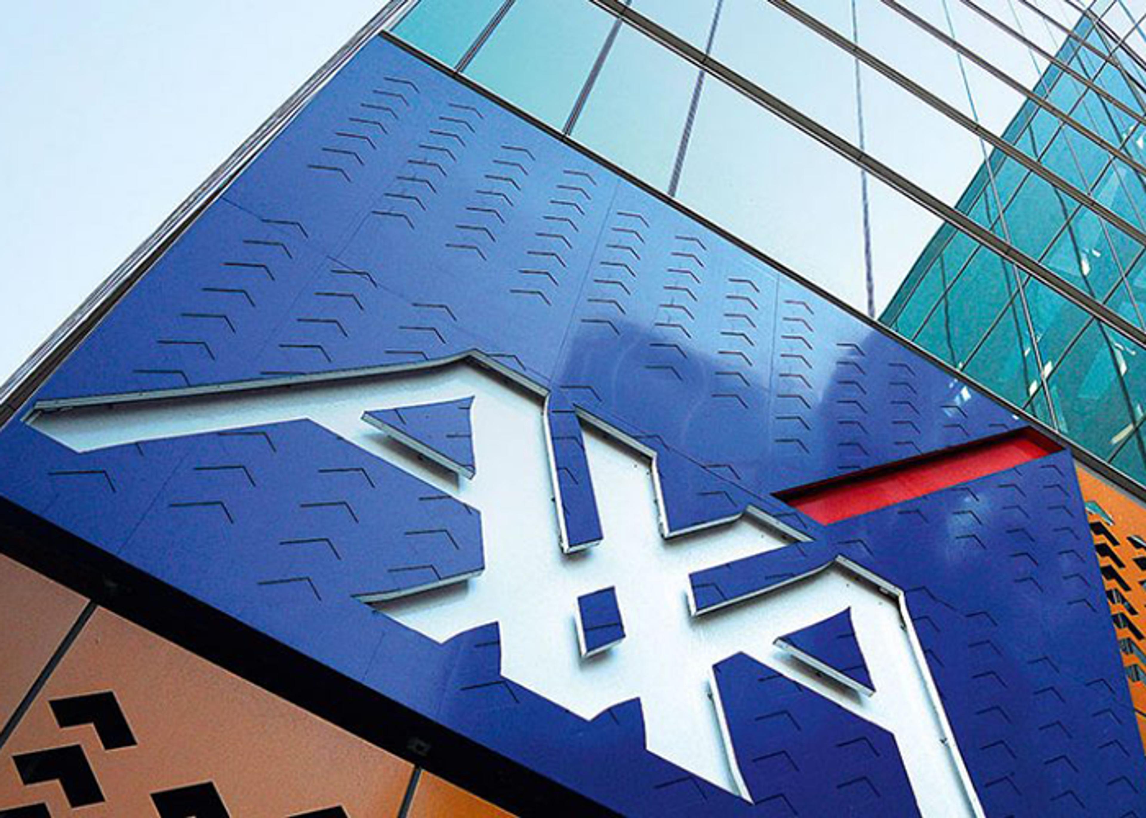 A close-up of a modern building facade featuring a blue and orange geometric design with a prominent logo in white. The reflective glass and textured surfaces highlight contemporary architectural elements.