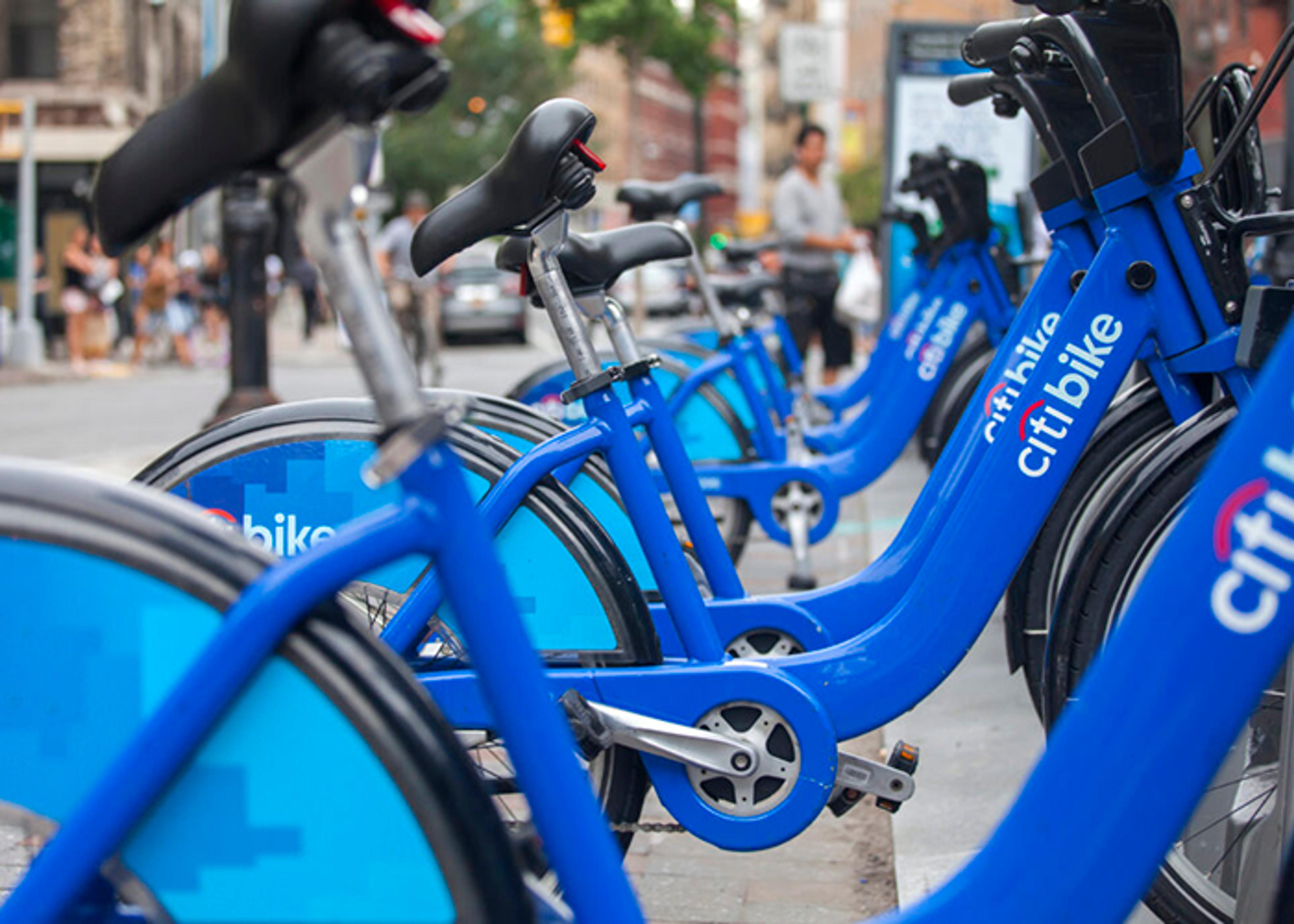 Row of blue rental bicycles parked on a city street; the nearest bike is in focus, displaying the Citi Bike logo.
