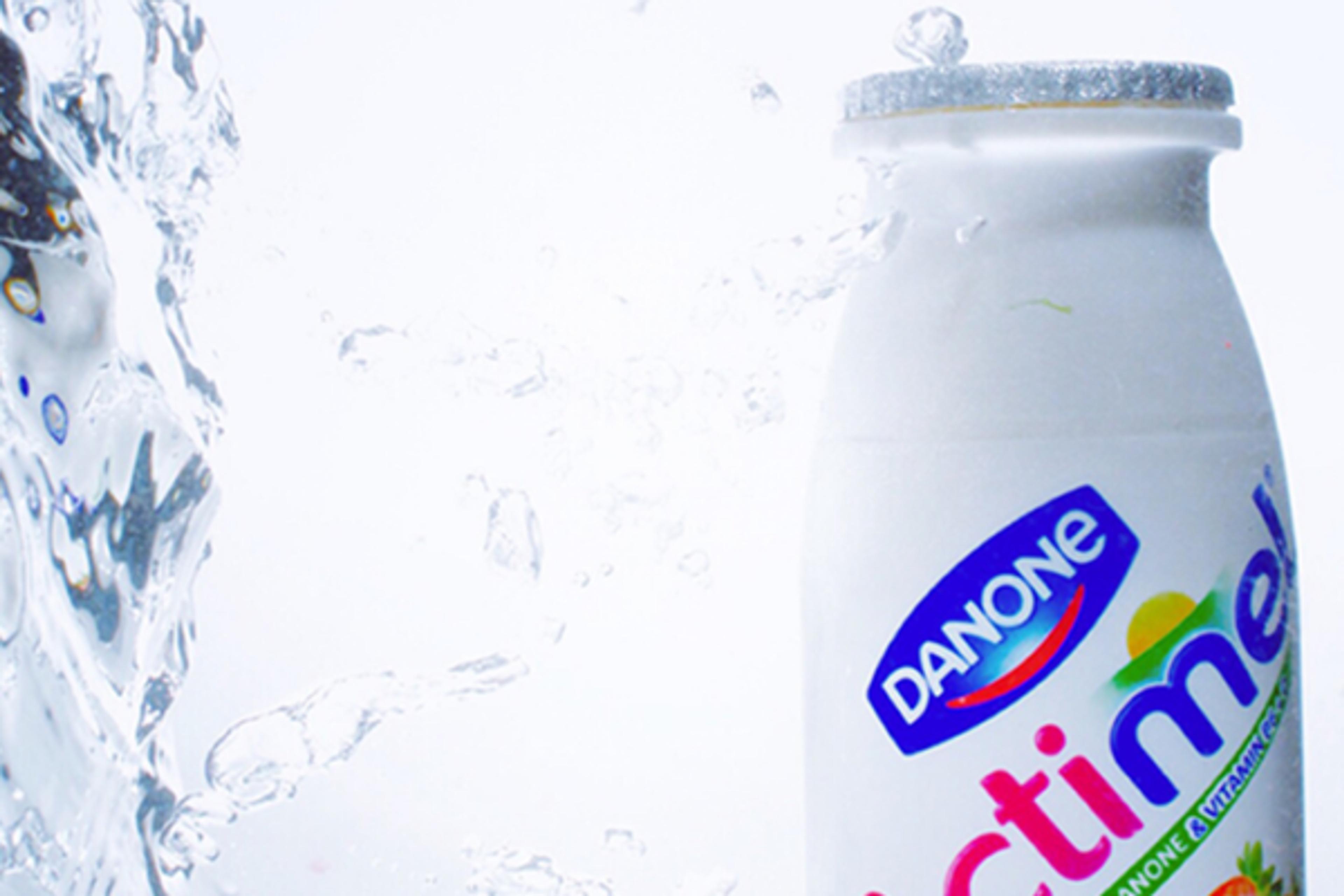 Danone Actimel bottle with water splashing around it on a white background.
