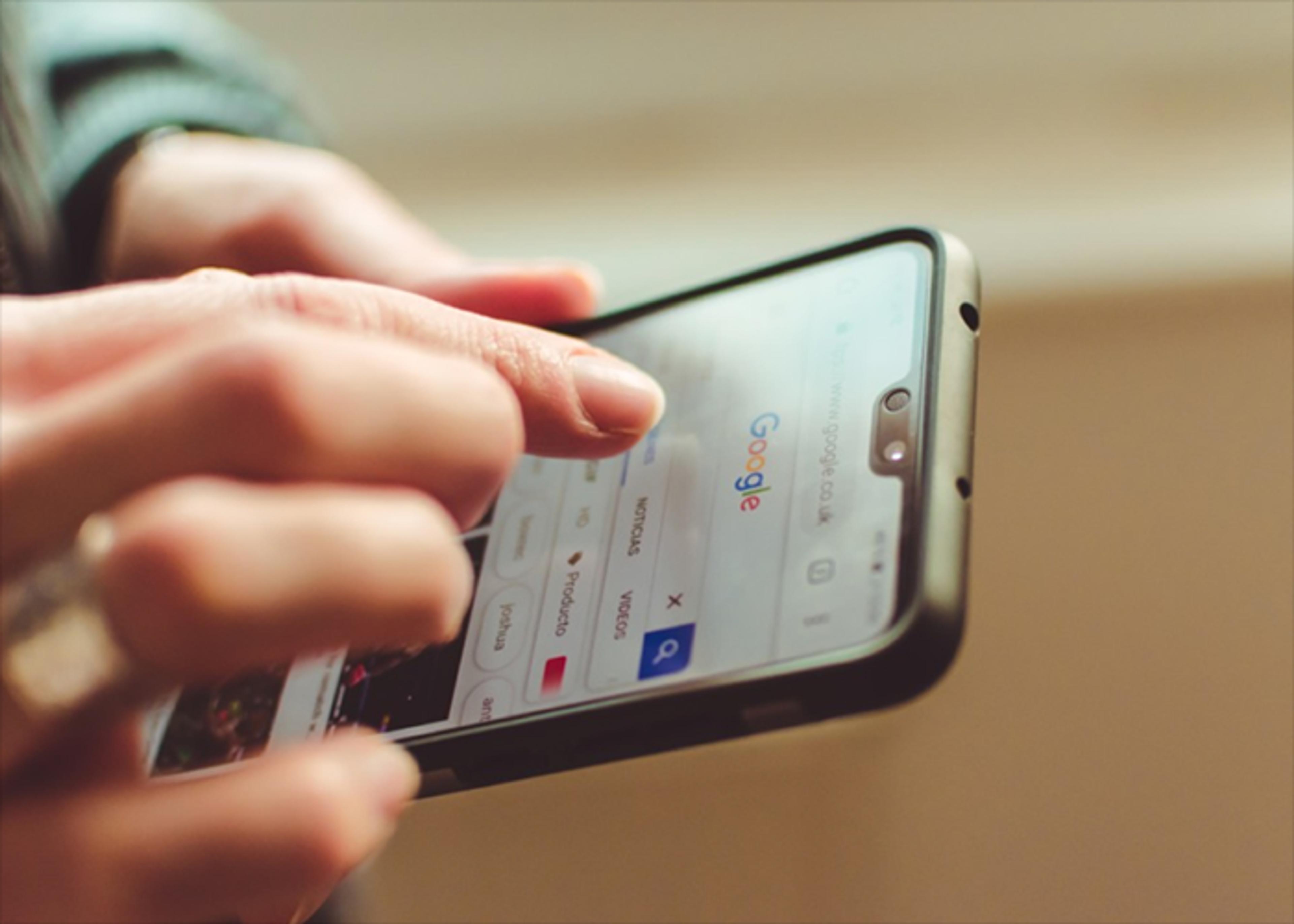 Close-up of a person's hands using Google Search on a smartphone.