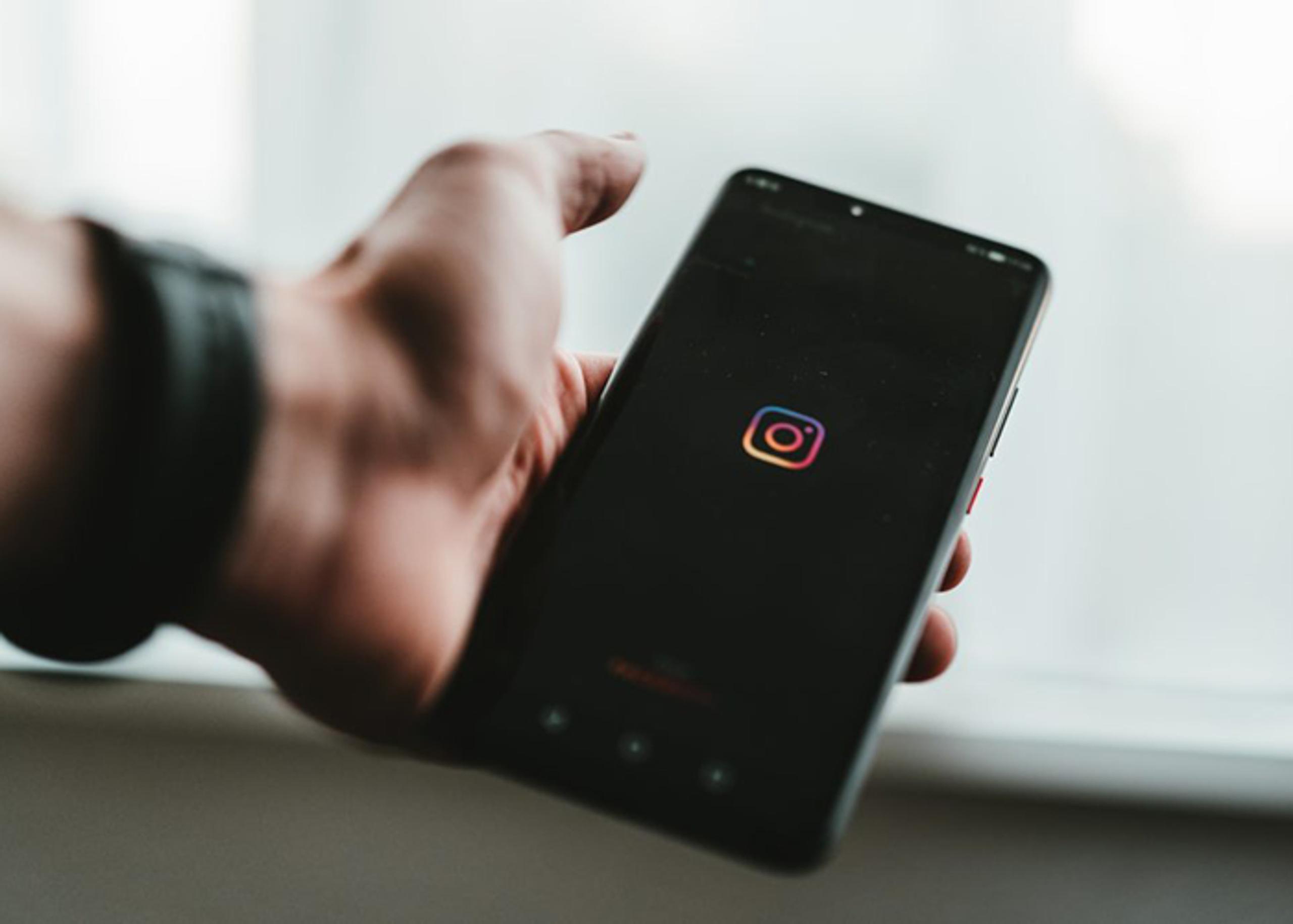 Hand holding a smartphone displaying the Instagram logo on a dark screen.