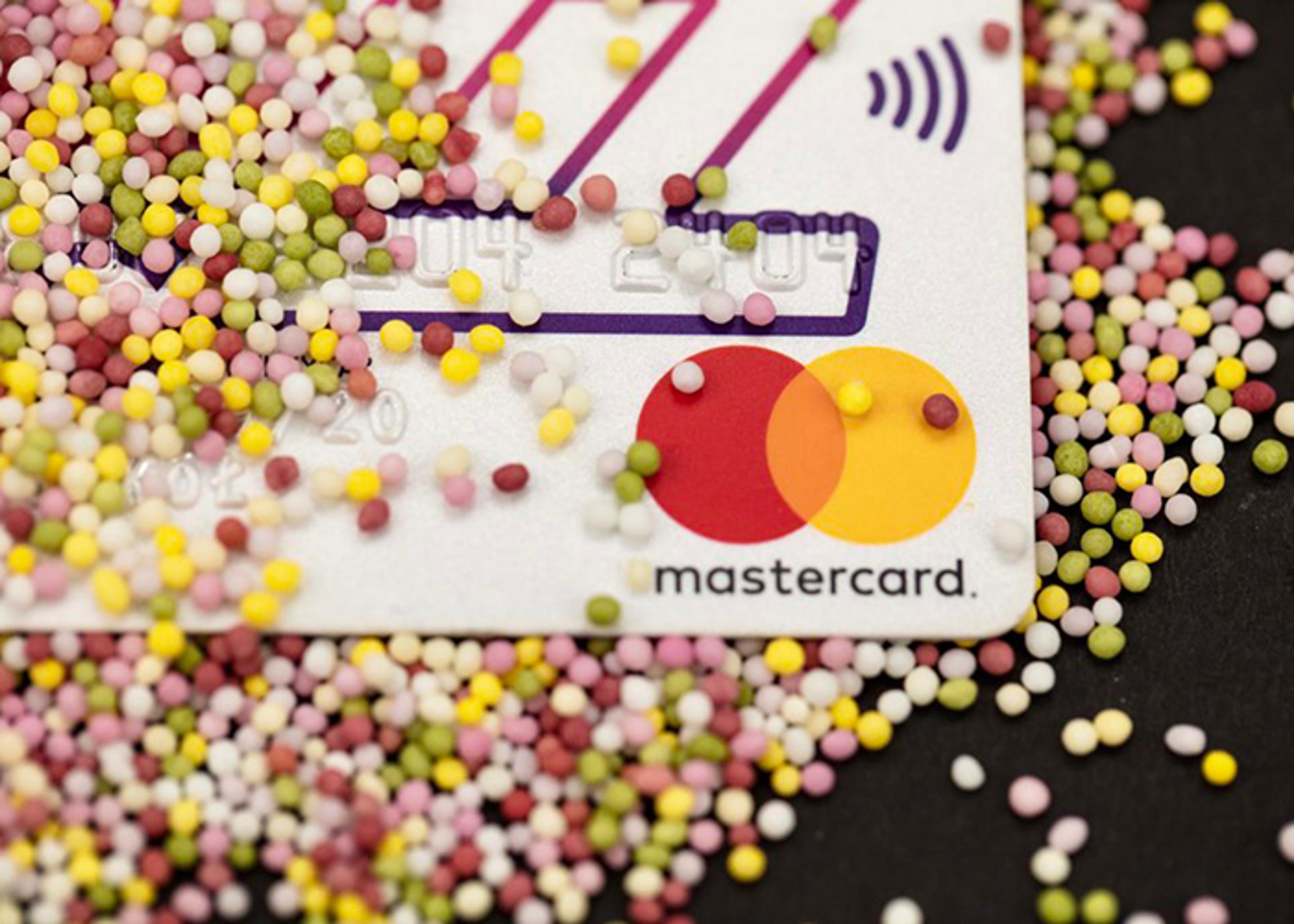 Close-up of a Mastercard credit card partially covered with multicolored sprinkle candies.