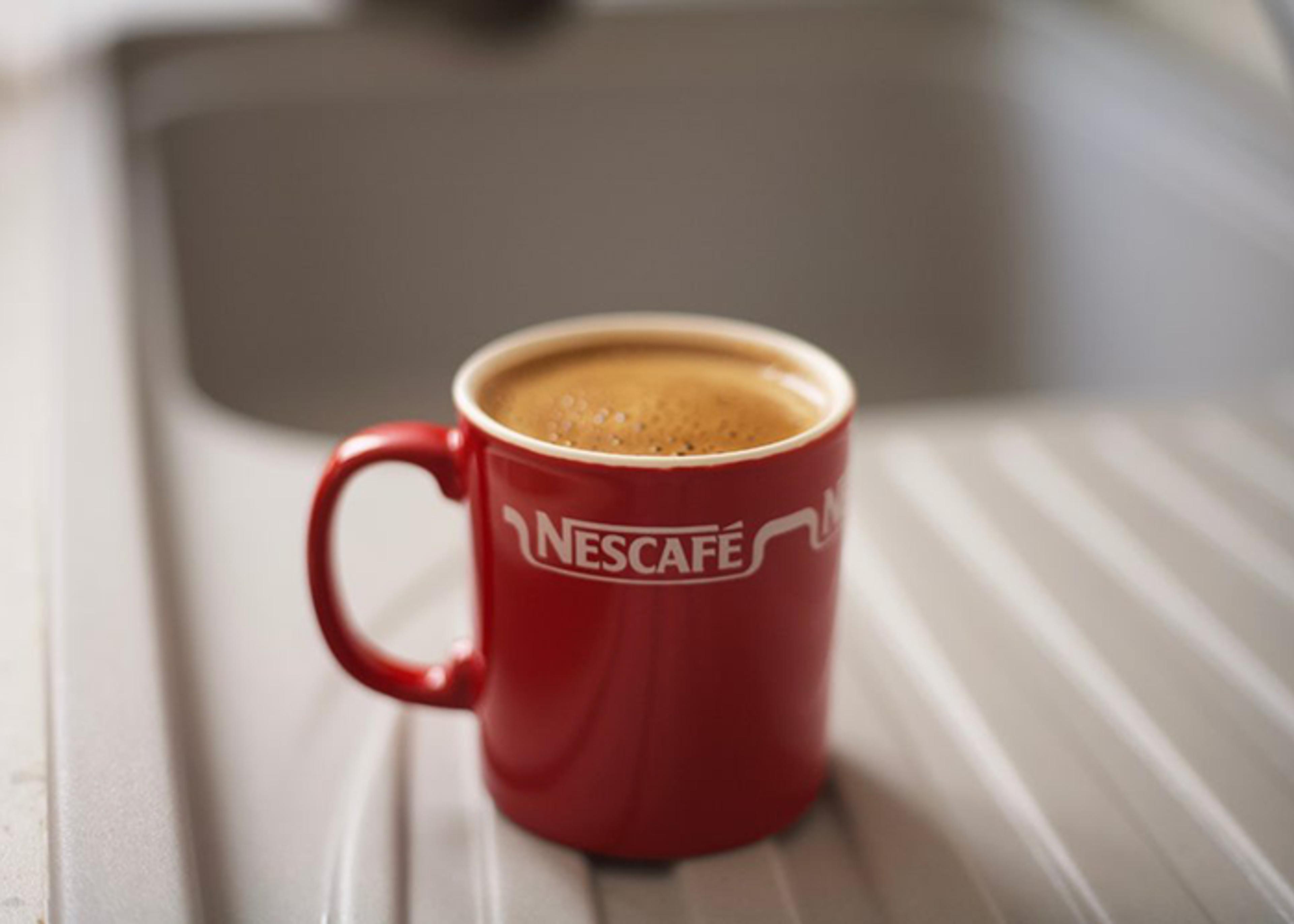 Close-up of a red Nescafe mug filled with coffee, resting in a white sink.