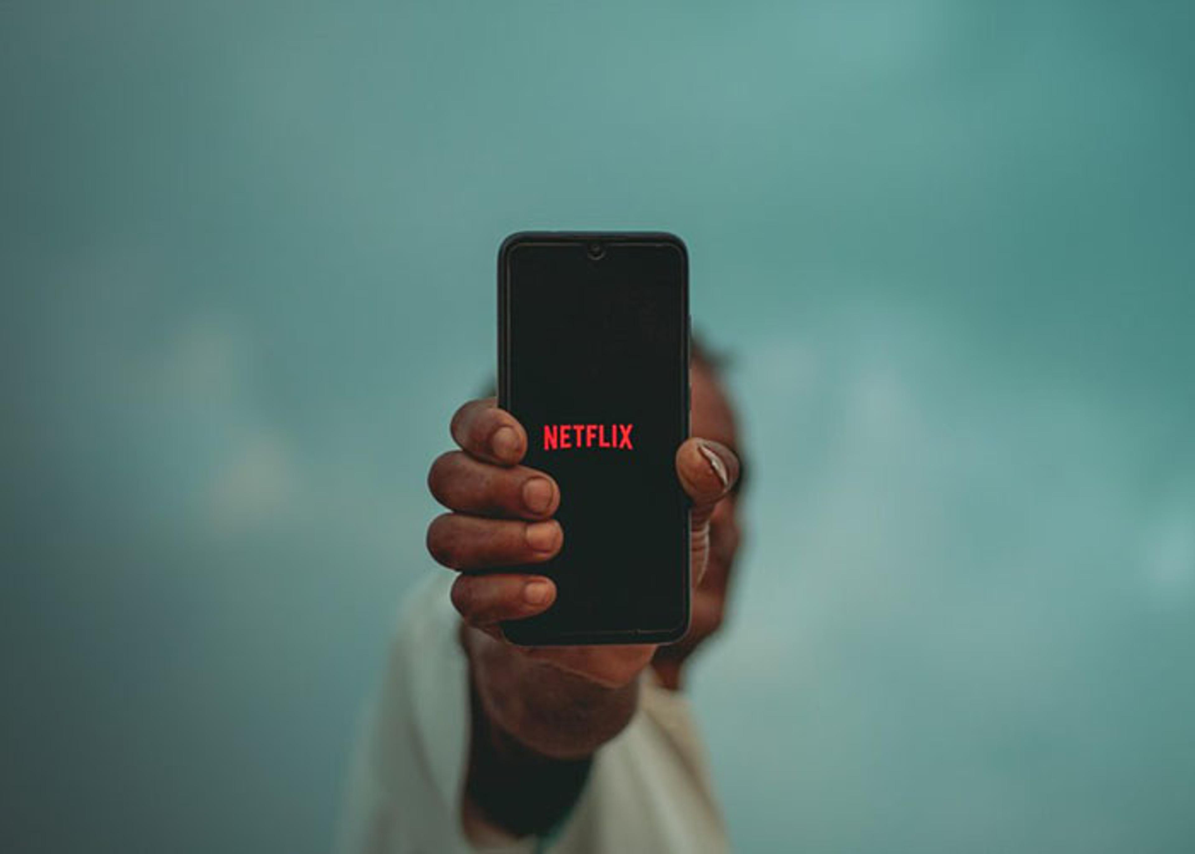 Hand holding a mobile phone displaying the Netflix logo.