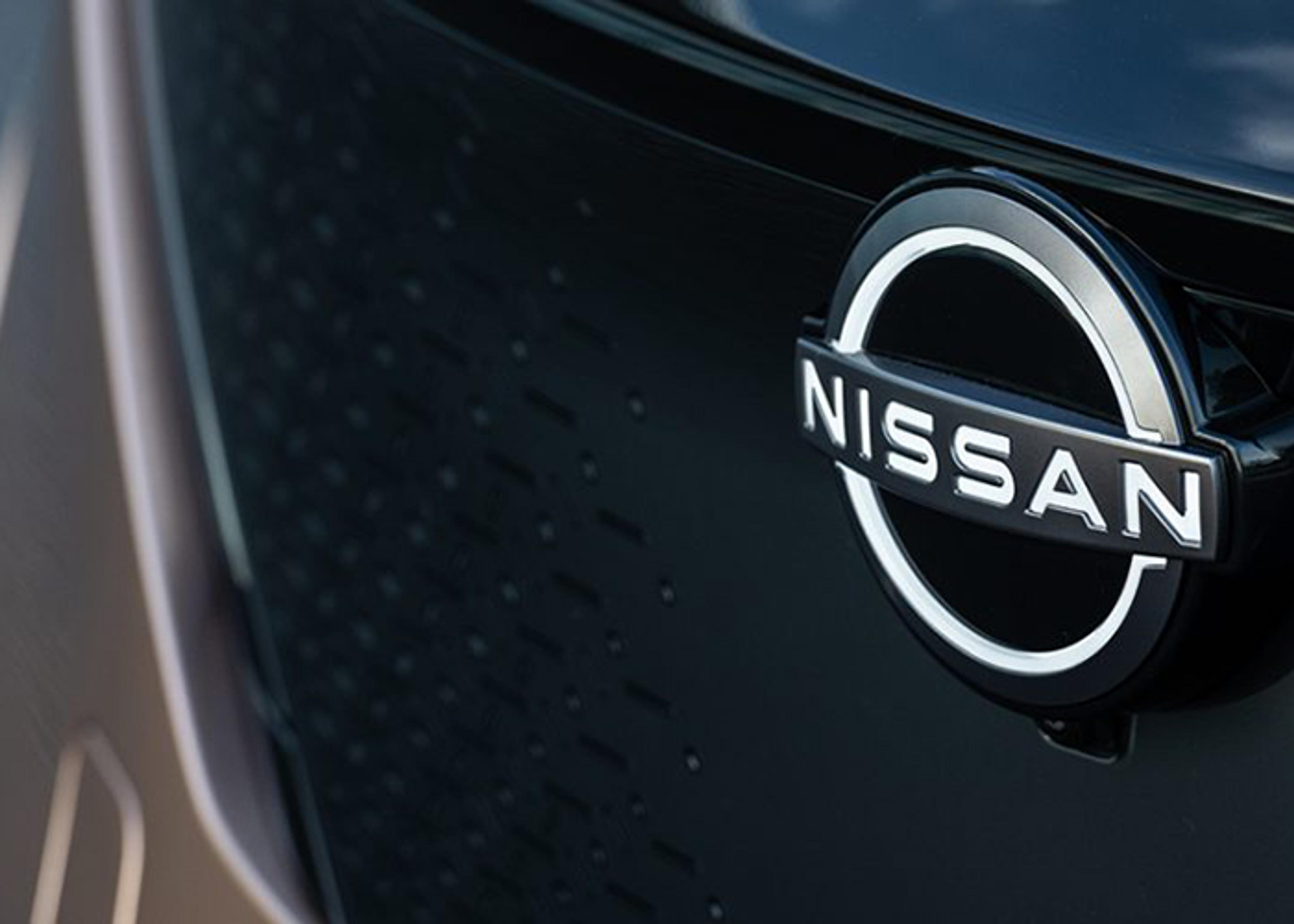 Close-up of a dark-colored Nissan vehicle's emblem which features the Nissan logo and brand name in silver.