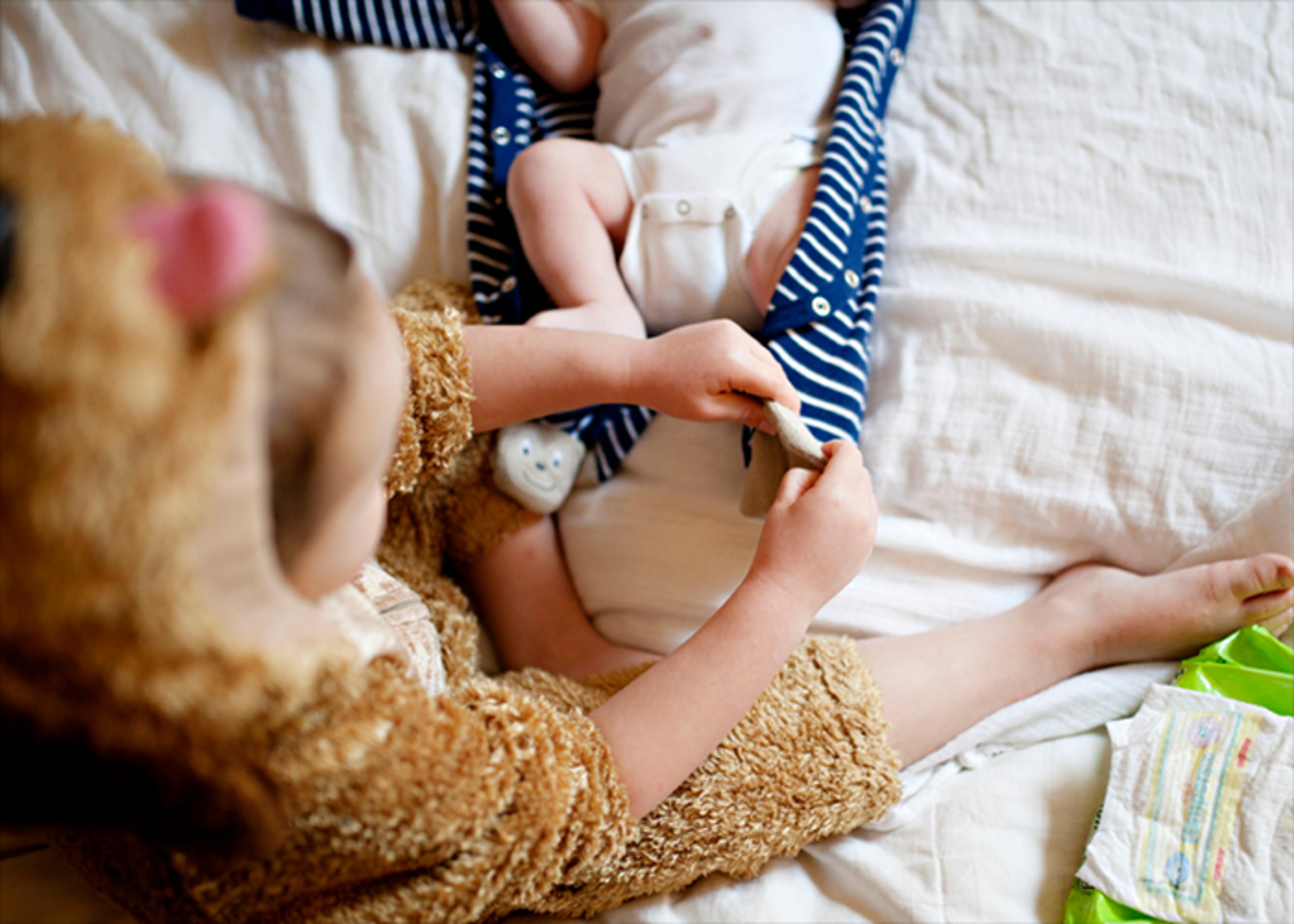 Child in a bear costume changes a baby’s diaper on a white blanket.