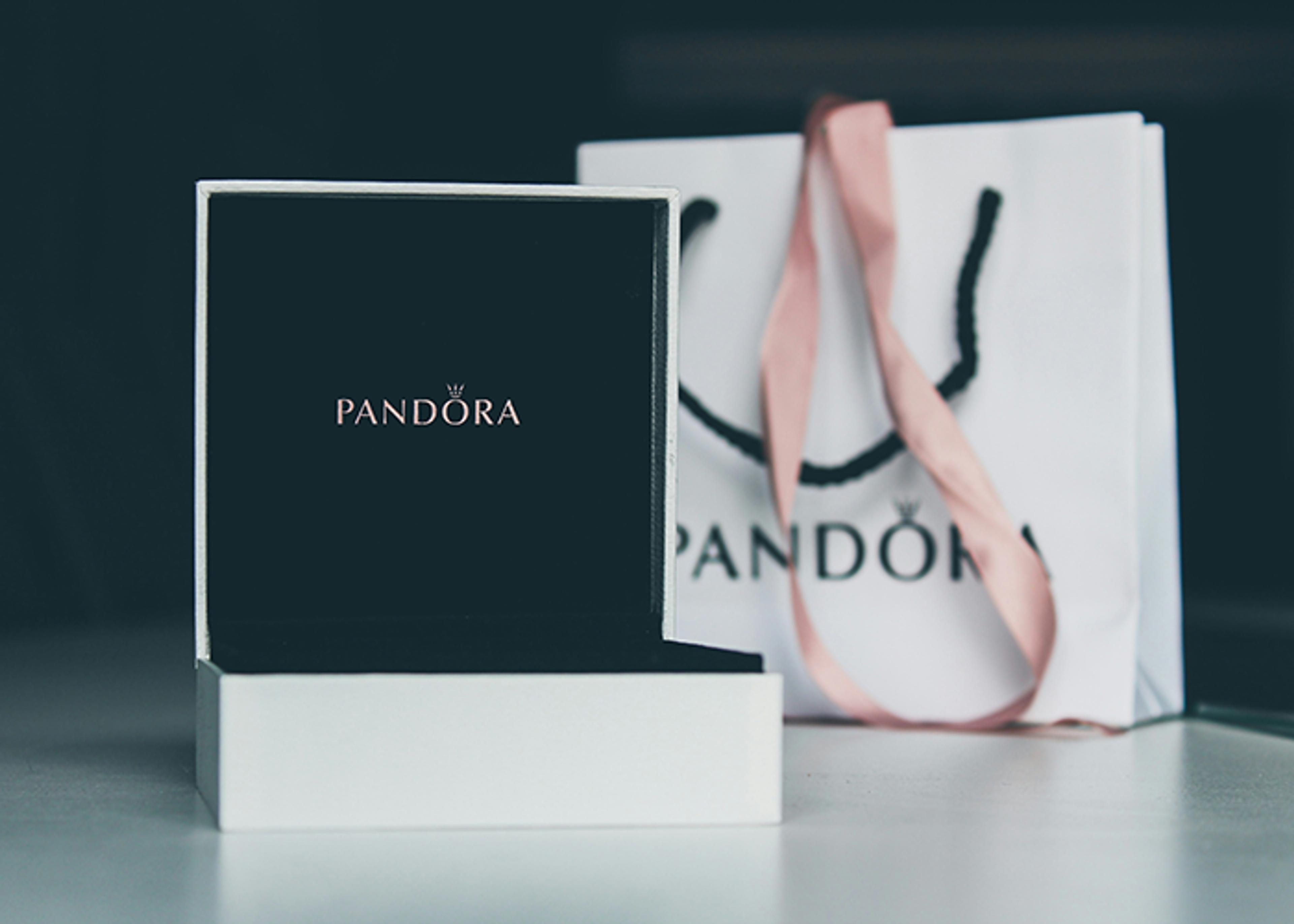 Open Pandora jewelry box next to a Pandora shopping bag with pink ribbon handles.