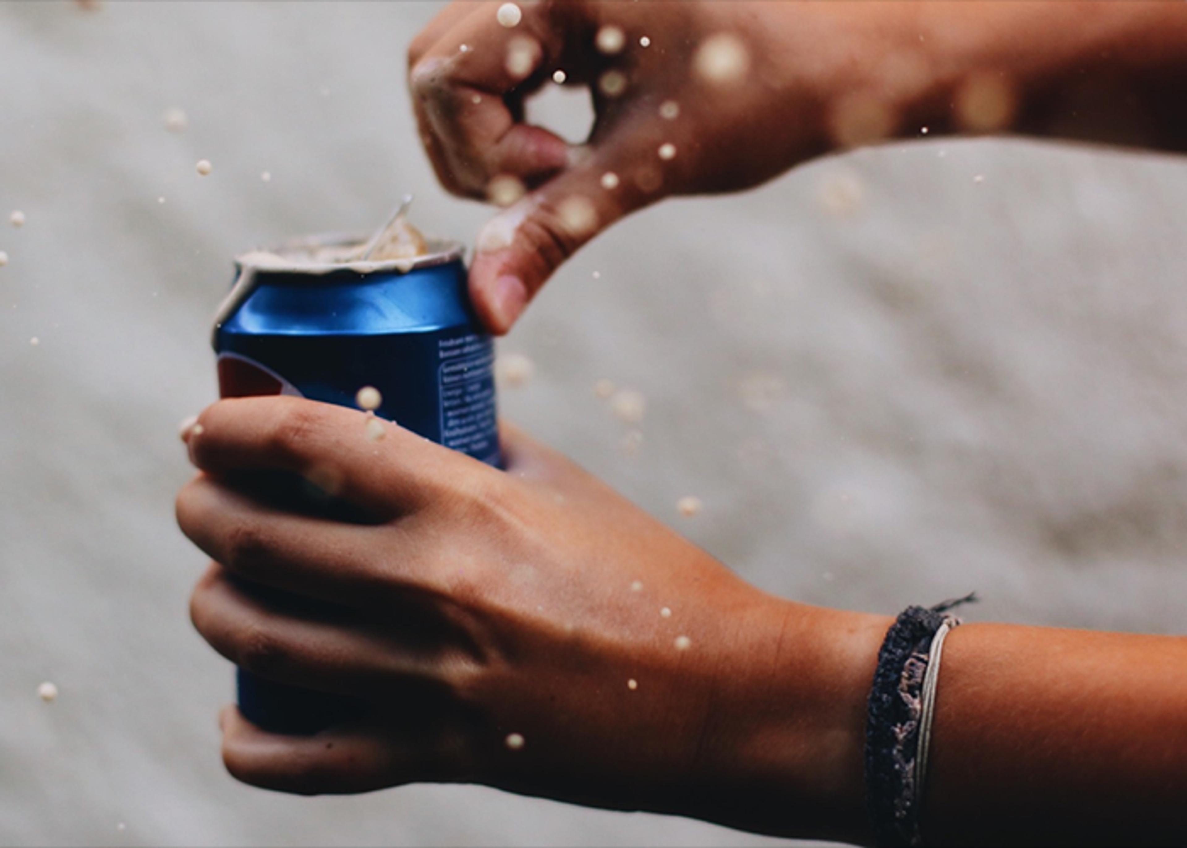 Hands opening a blue Pepsi can, with liquid spraying.