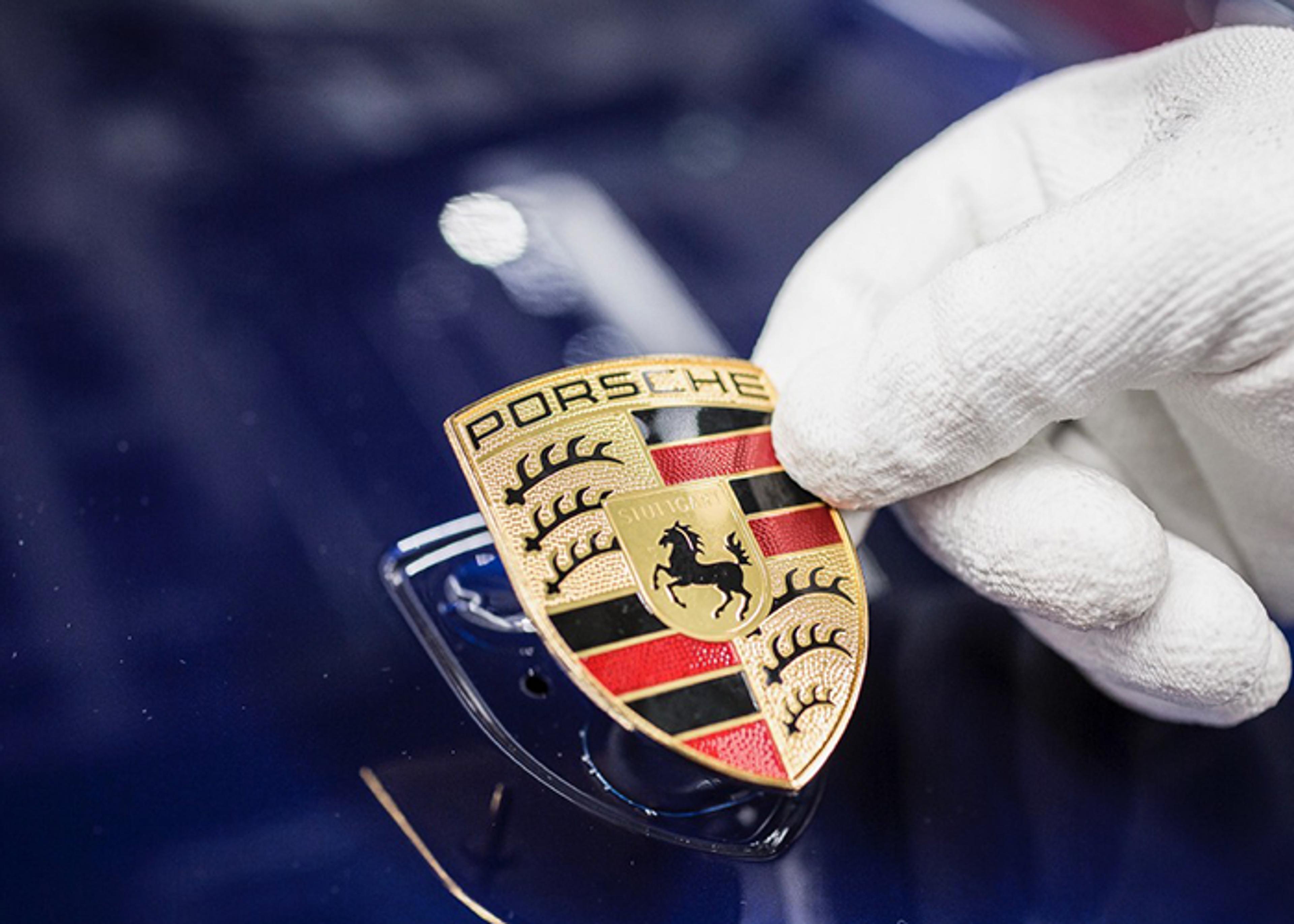 Hand in white glove holding a Porsche crest over a blue car body.