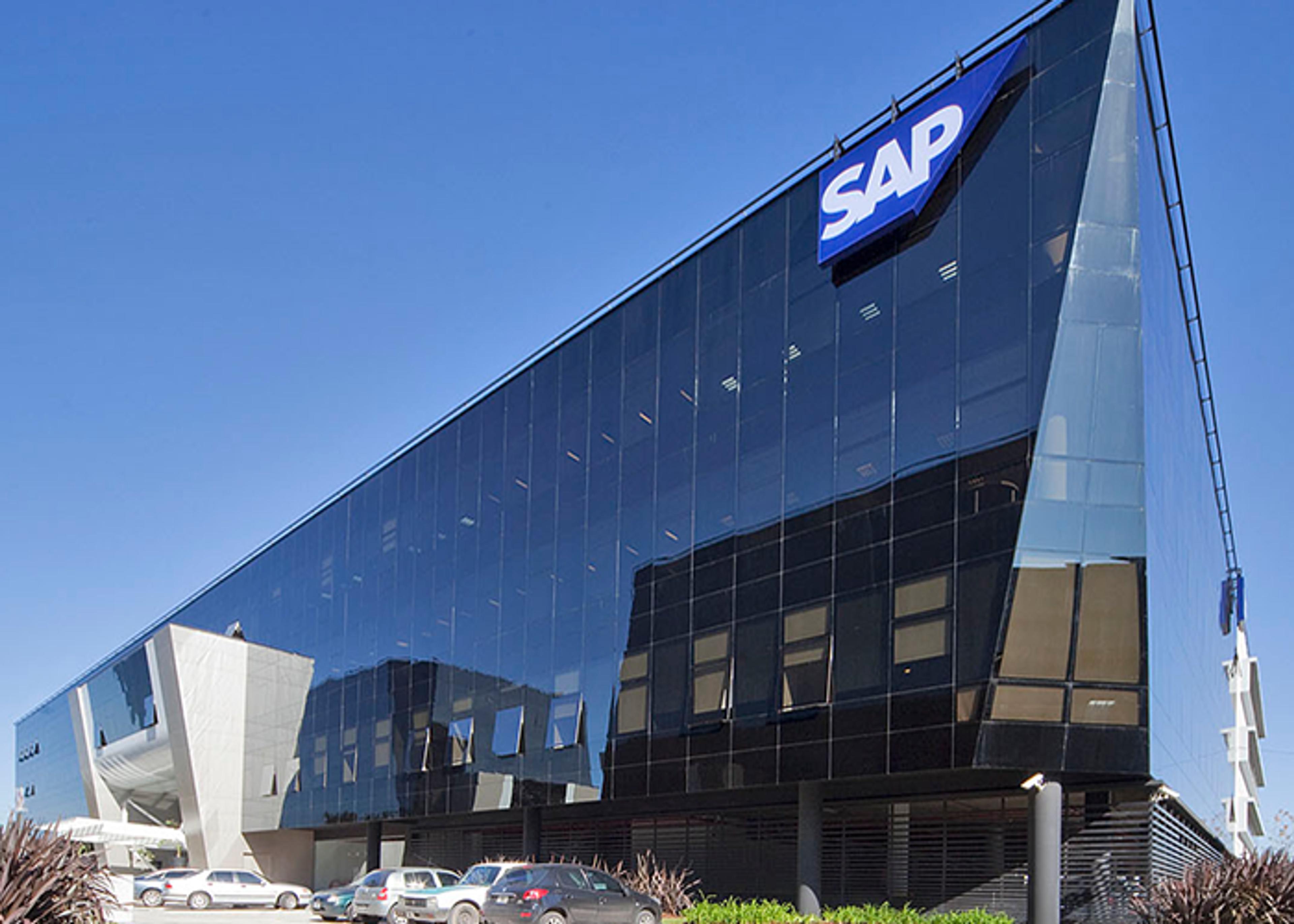 Exterior view of modern, angular office building with a glass facade, marked with the SAP logo. Cars are parked in front of the building.