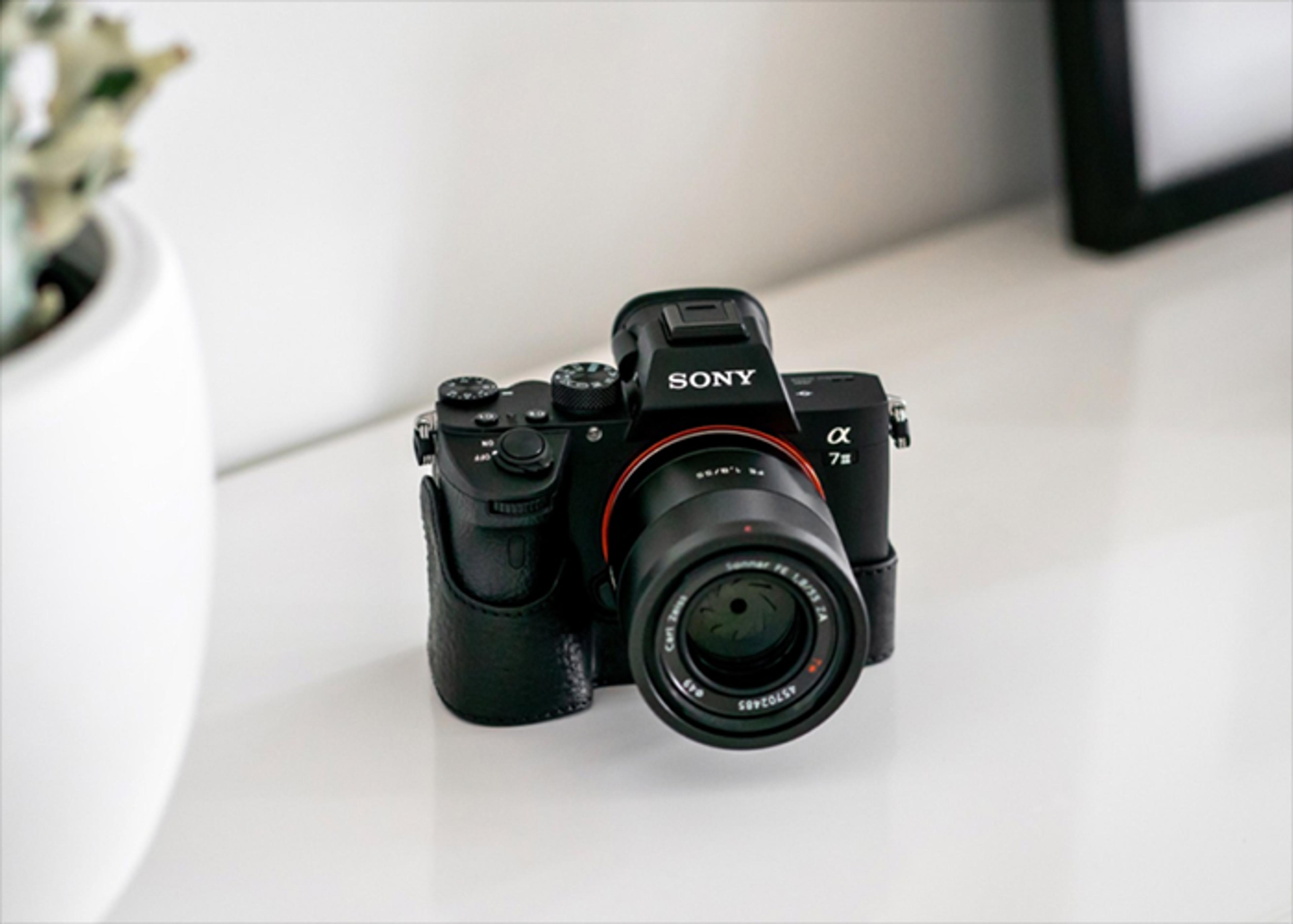 A black Sony Alpha 7S camera with a Carl Zeiss lens sits on a white surface.