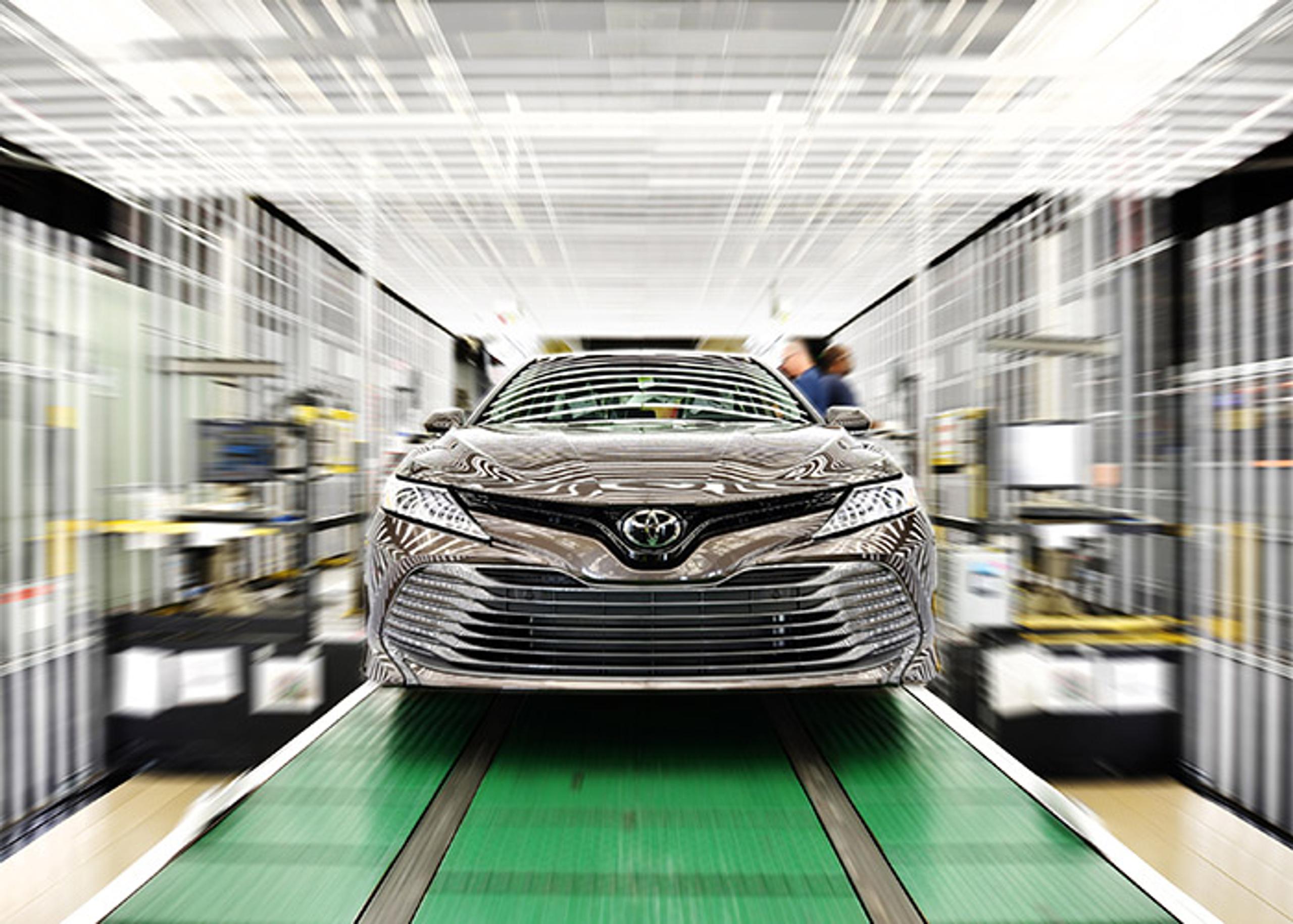 Automobile assembly line featuring a gray Toyota Camry on a green conveyor belt with blurred background.