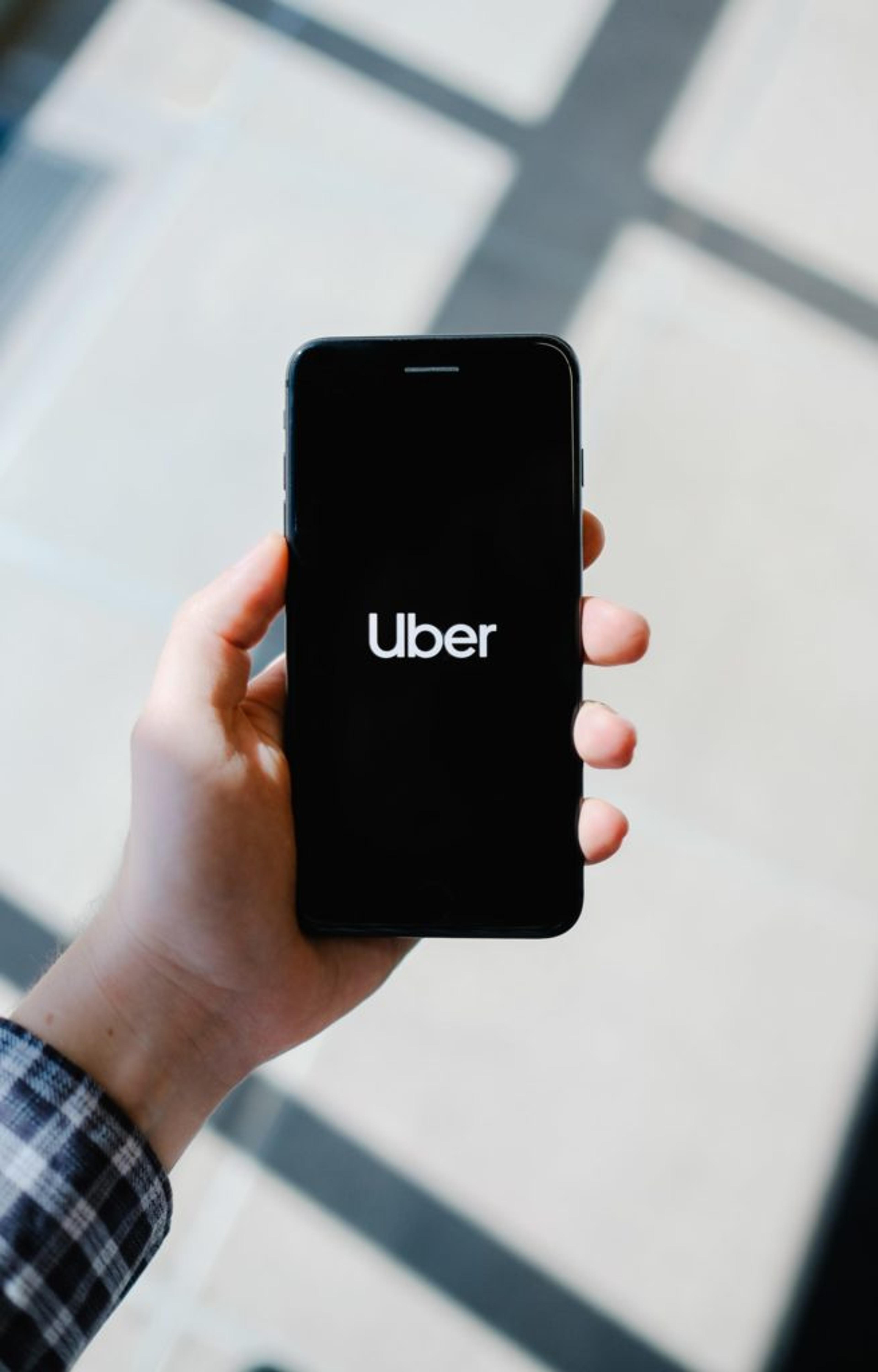 A human hand holds a smartphone displaying the Uber logo against a background of light and shadow.