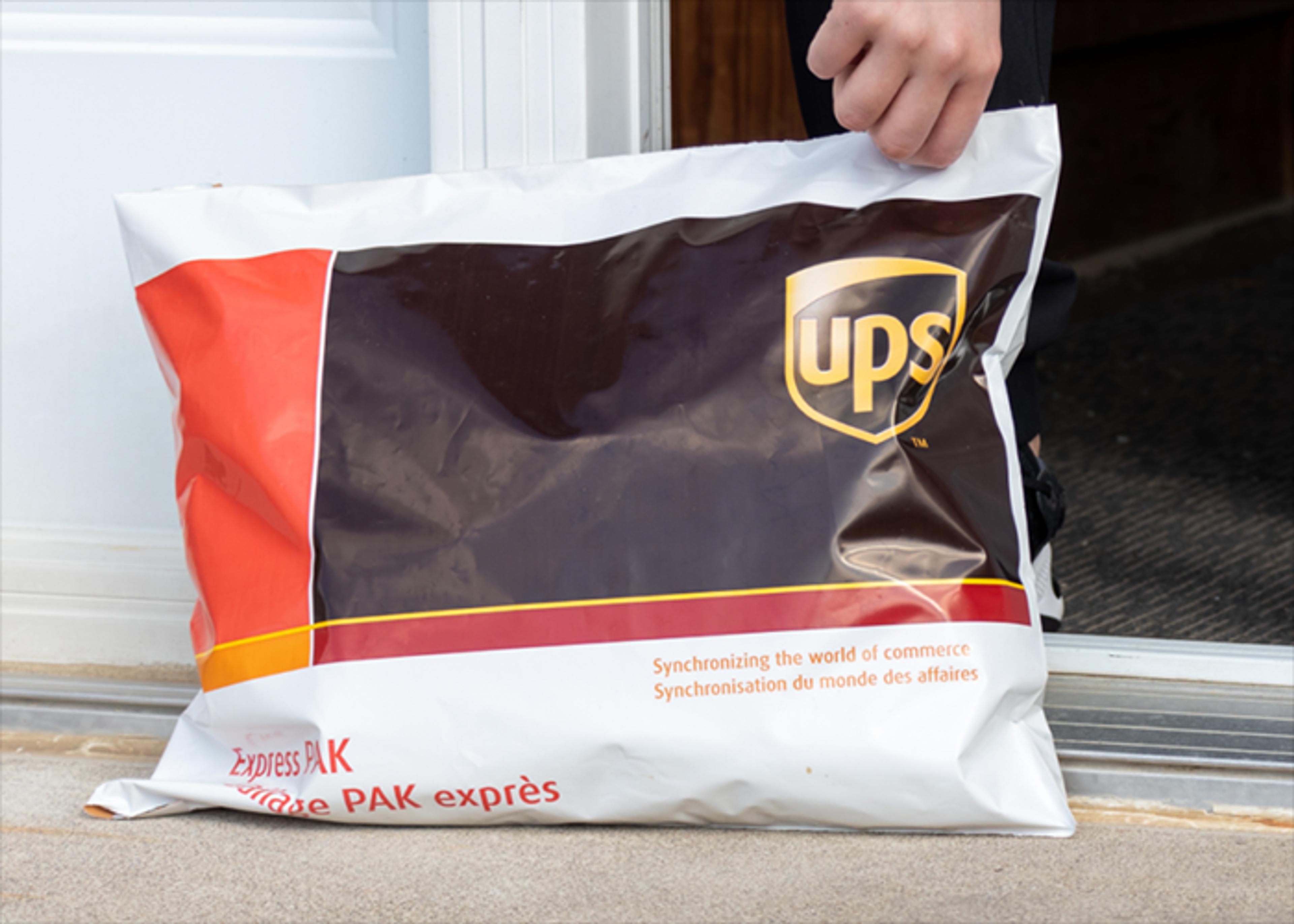 A UPS Express PAK lies on a doorstep, partially held by a person off-screen.