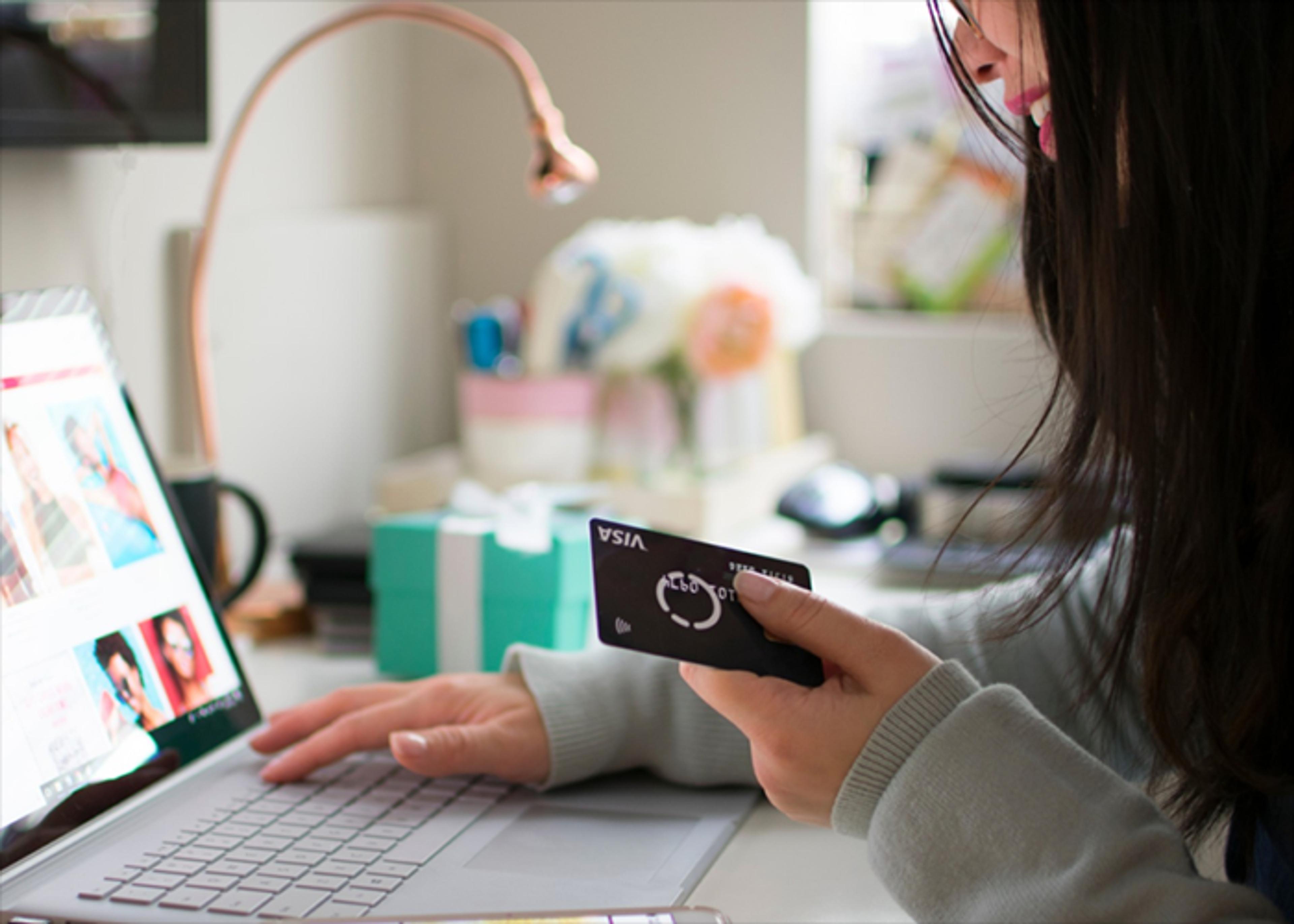 Woman smiling while online shopping, holding a black Visa card as her other hand types information into a laptop.