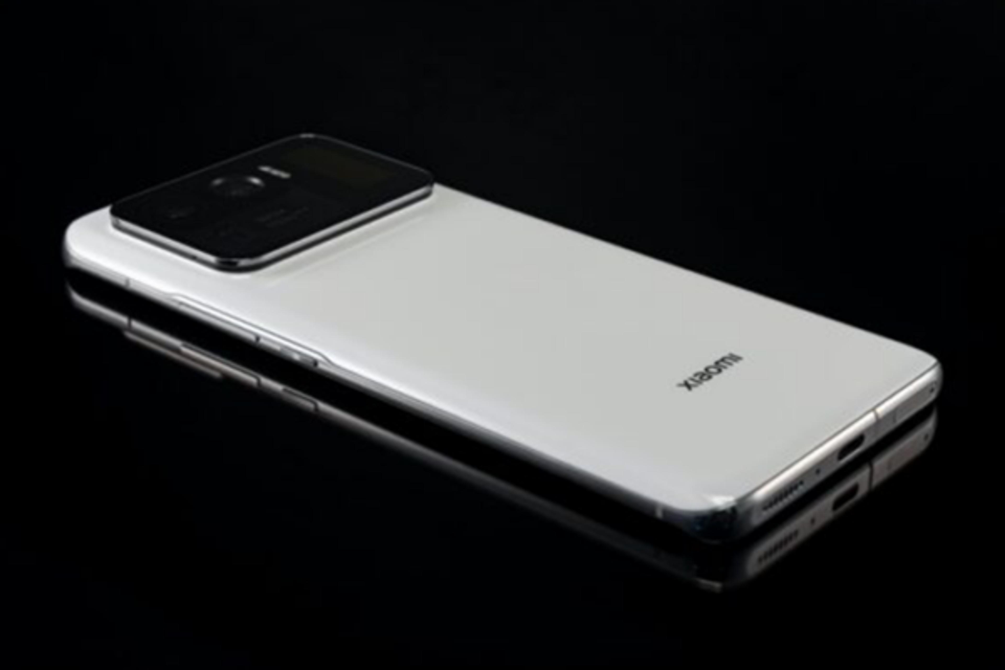 Close-up of a Mi Xiaomi 12S Ultra smartphone, white in color, at a slight angle, with the camera bump visible, against a shiny black surface.