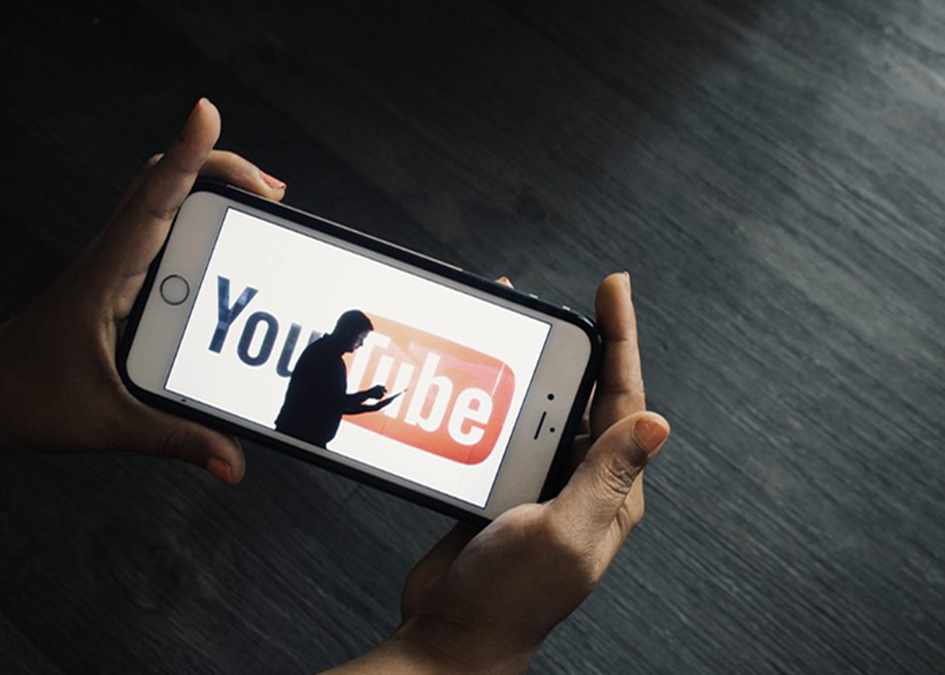 Hands holding a smartphone displaying the YouTube logo.