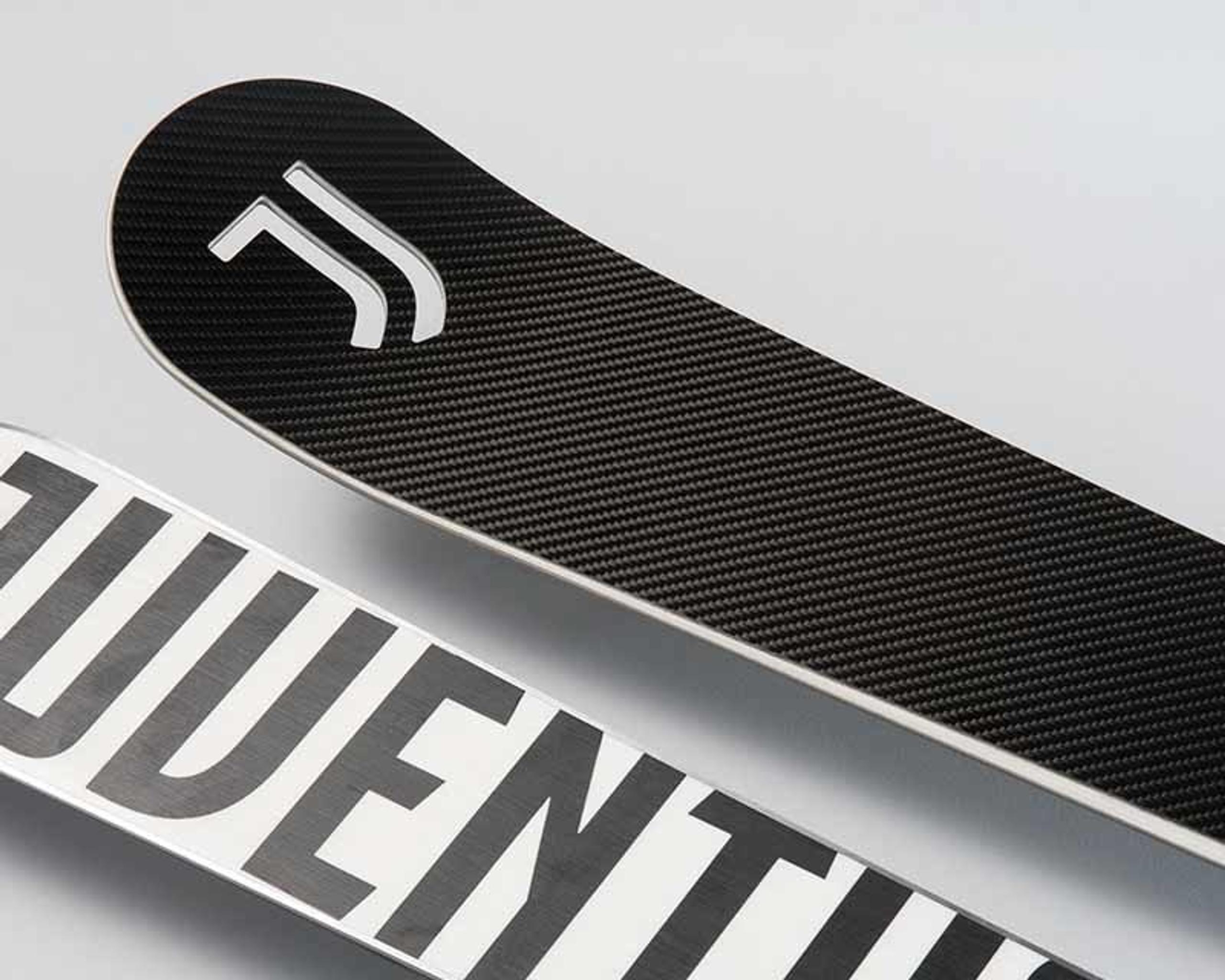Close-up of two skateboard decks; one with the Juventus logo on a carbon fiber texture, the other showing part of the word "Juventus" in large, white letters outlined in black.