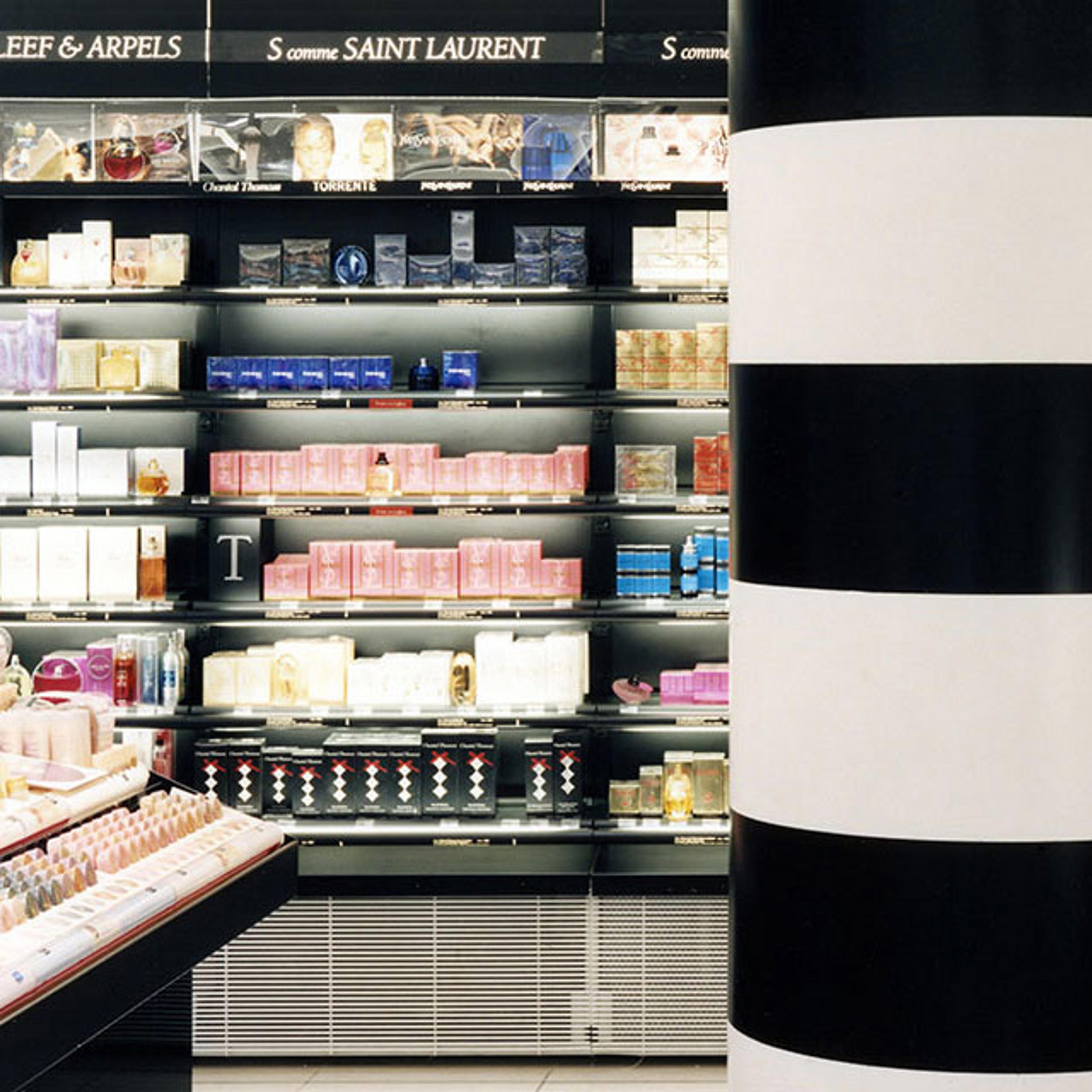 Interior view of a cosmetic and fragrance display in a store, featuring shelves stocked with various perfume and cosmetic products, and a black-and-white striped column.