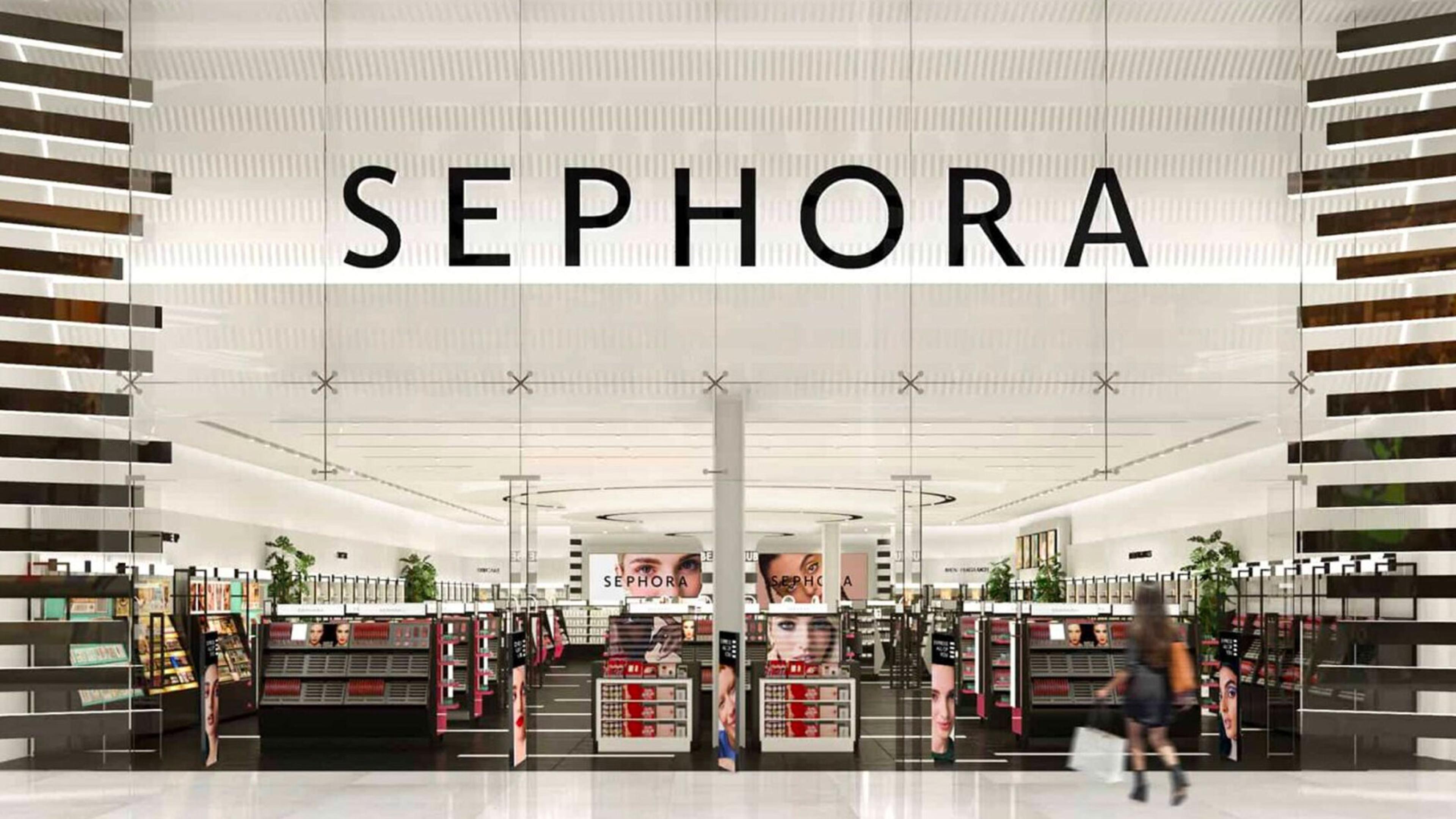 Exterior of a Sephora retail store, showcasing the brand's logo prominently displayed above the entrance, with cosmetic displays visible within. A blurred figure of a woman is walking inside the store.