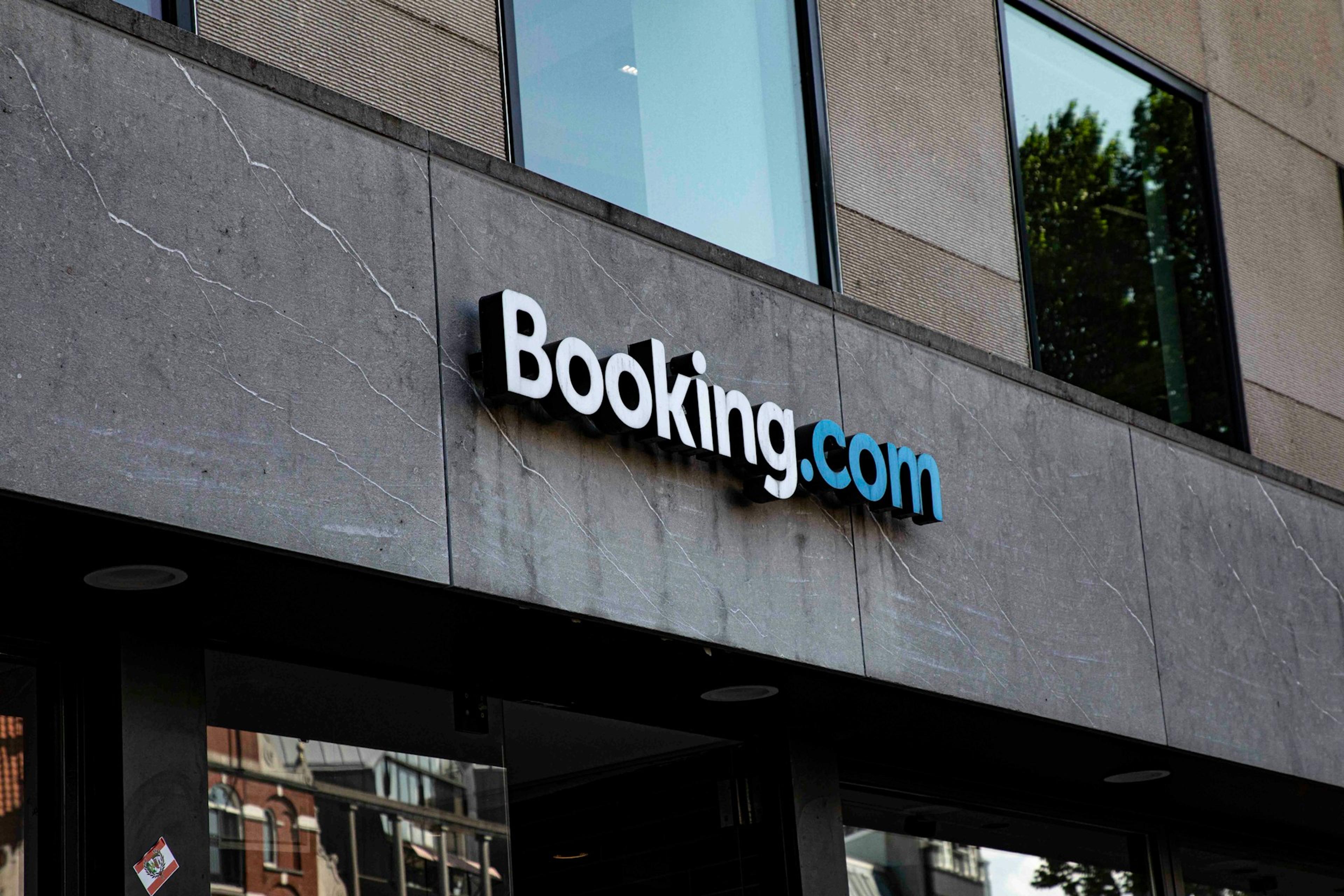 Booking.com sign on a gray concrete building facade above a glass entrance.