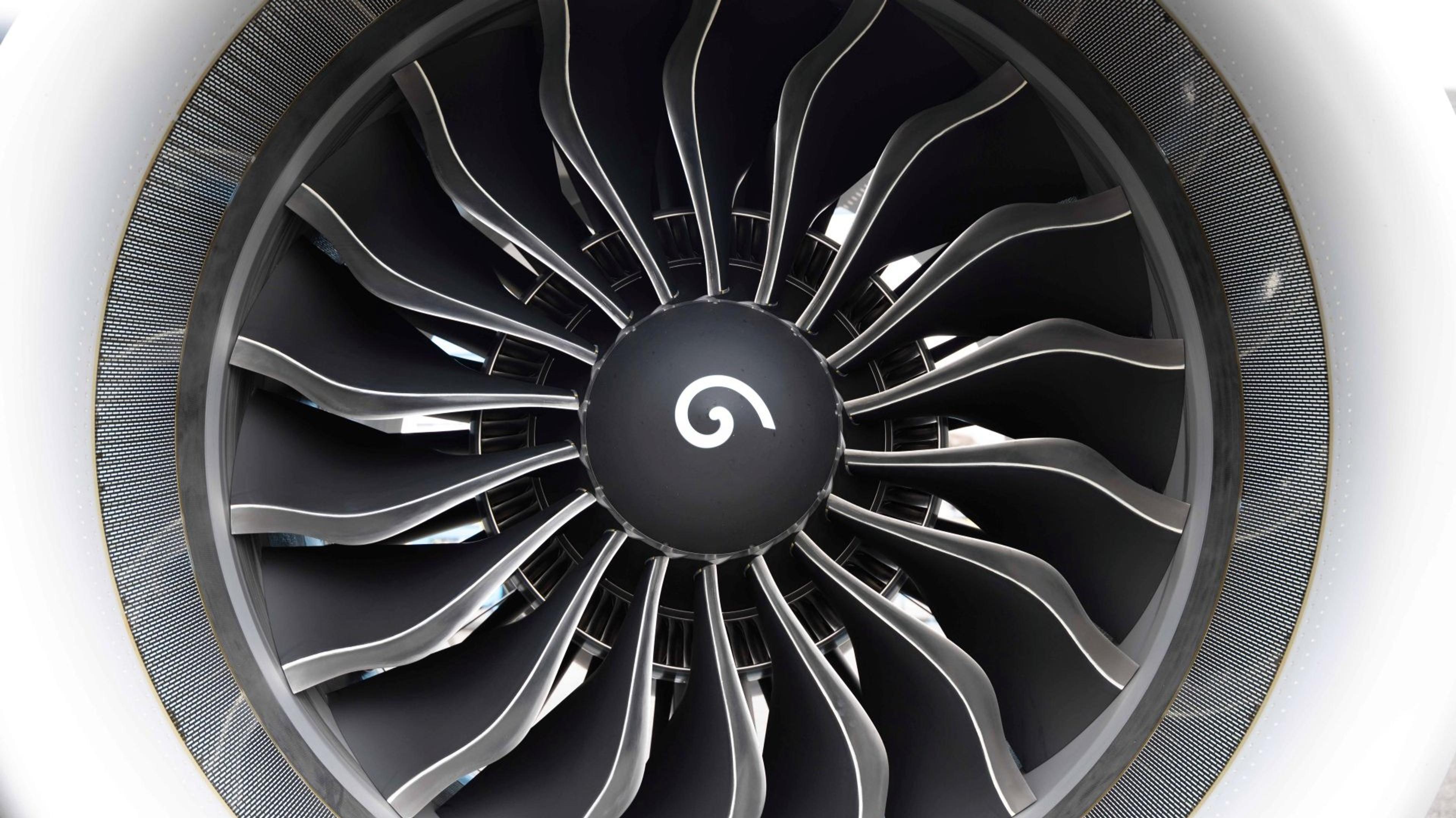 Close-up of a jet engine with black blades radiating from a central hub, and a white spiral logo centrally located on the hub.