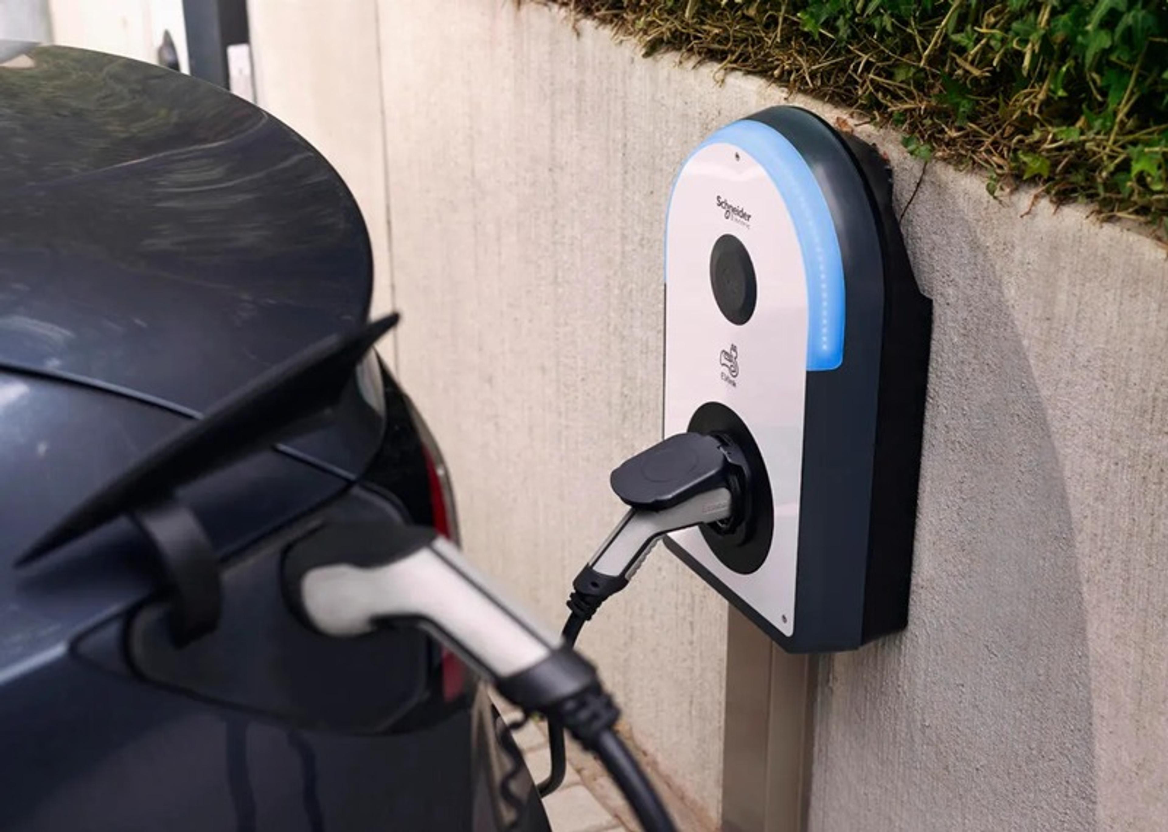 Electric car connected to a Schneider Electric charging station, mounted on a concrete wall.