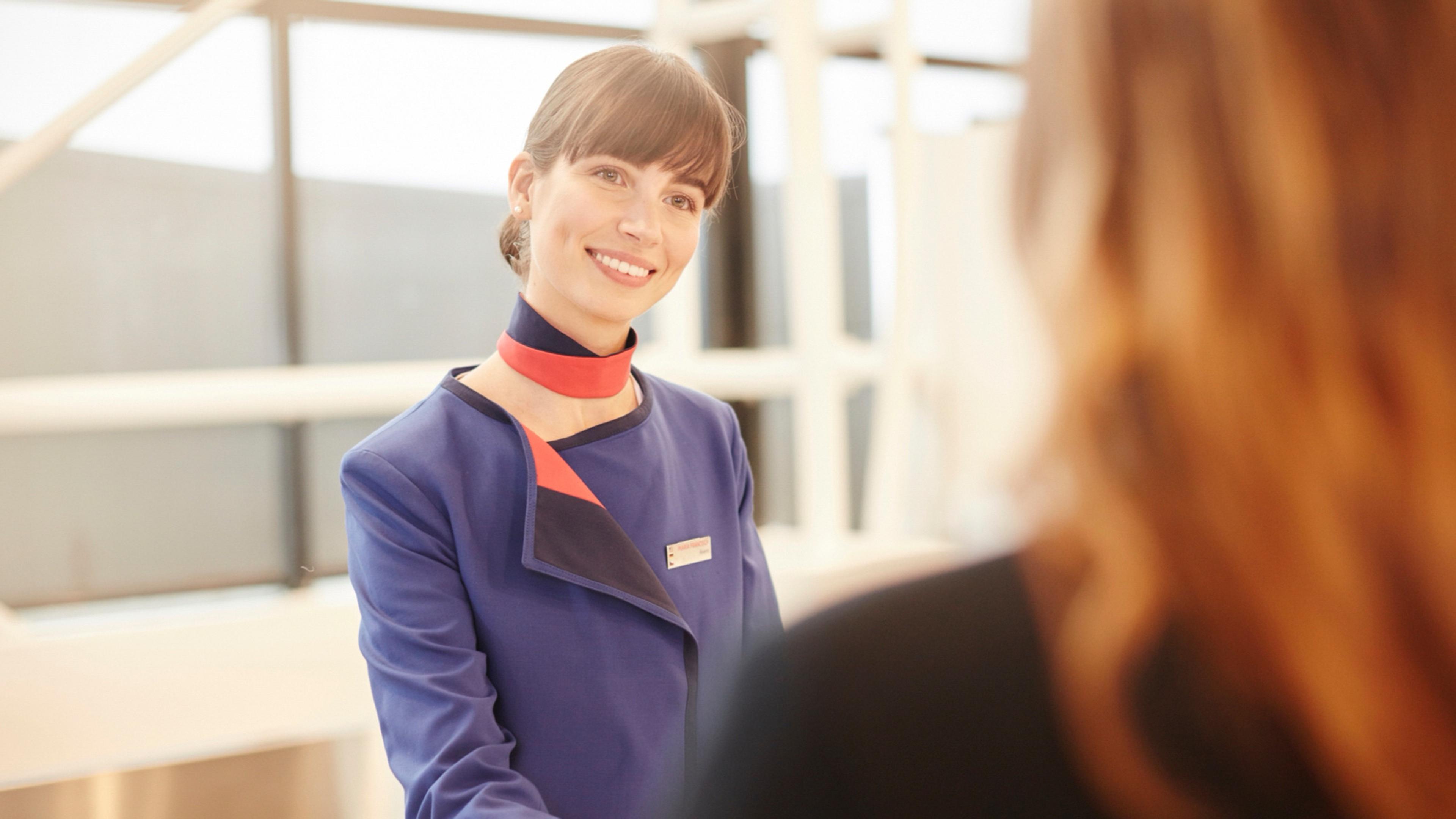 Smiling LATAM Airlines employee wearing a blue uniform with a red scarf assists a passenger.