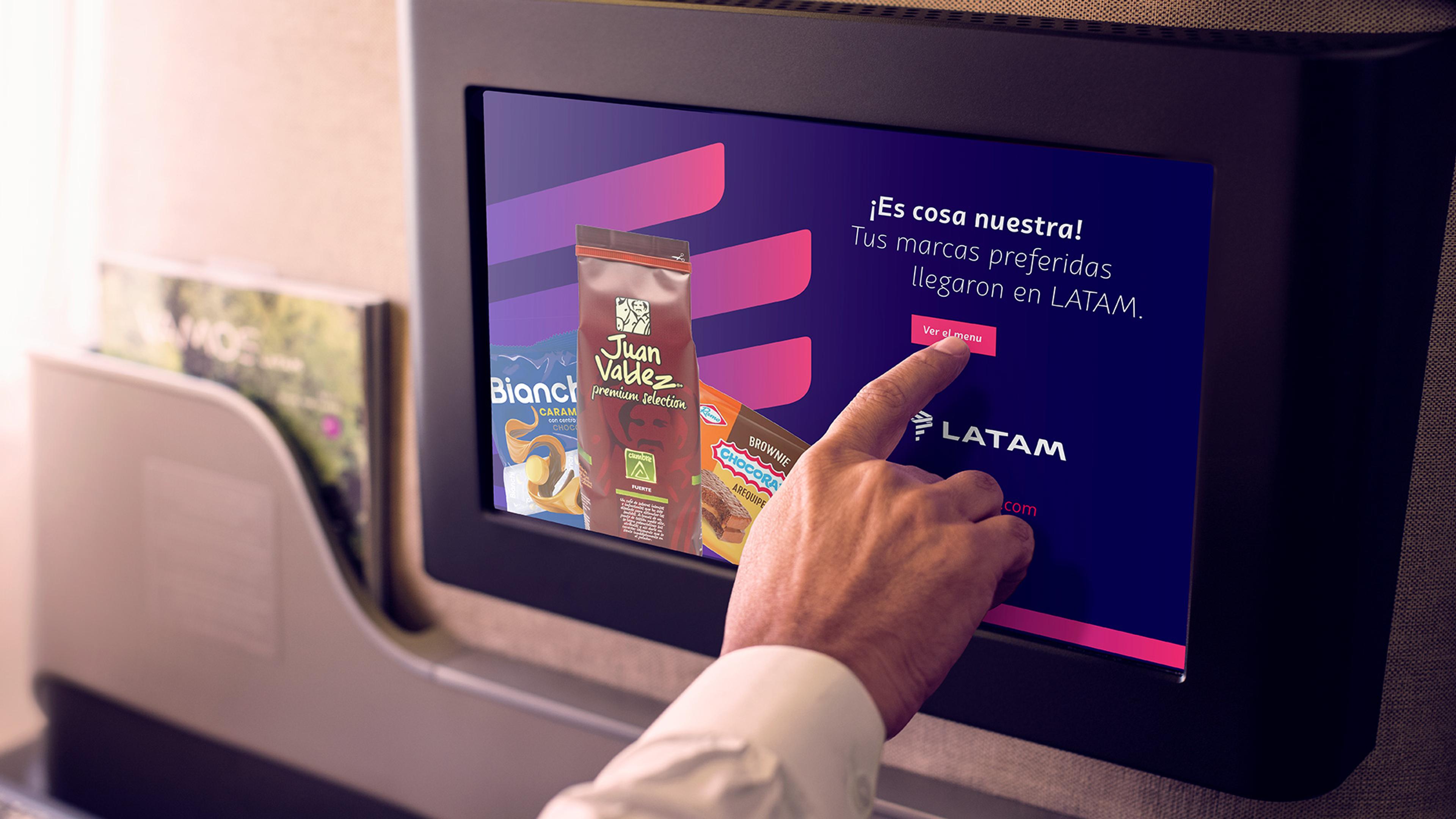 Close-up of airline inflight entertainment screen displaying snacks available for purchase, with hand touching "Ver el menu" button.