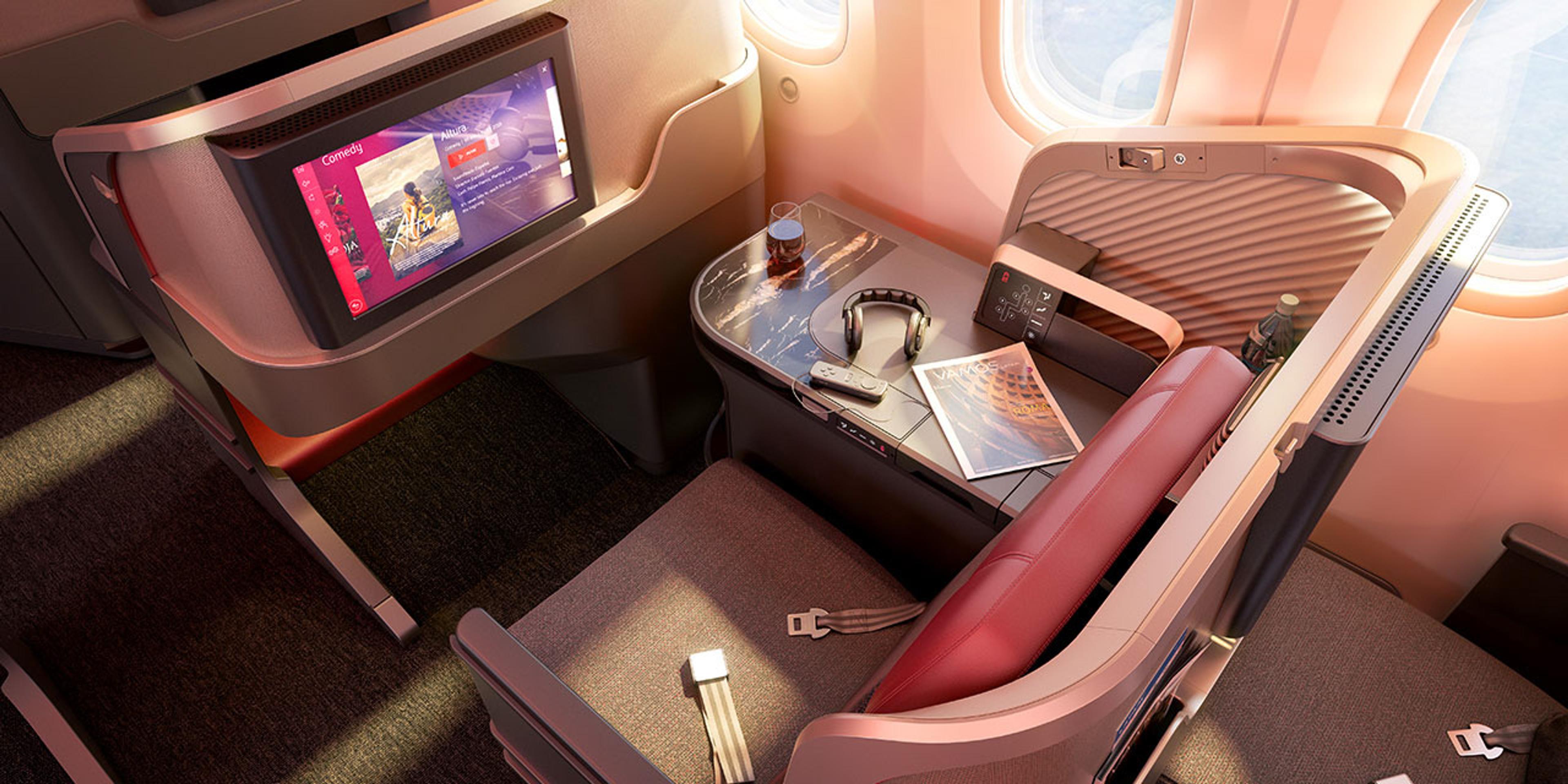 An unoccupied premium airline seat featuring a personal entertainment system displaying a comedy movie, a marbleized-surface side table with headphones, a partially-viewed magazine, and window with diffused natural light.