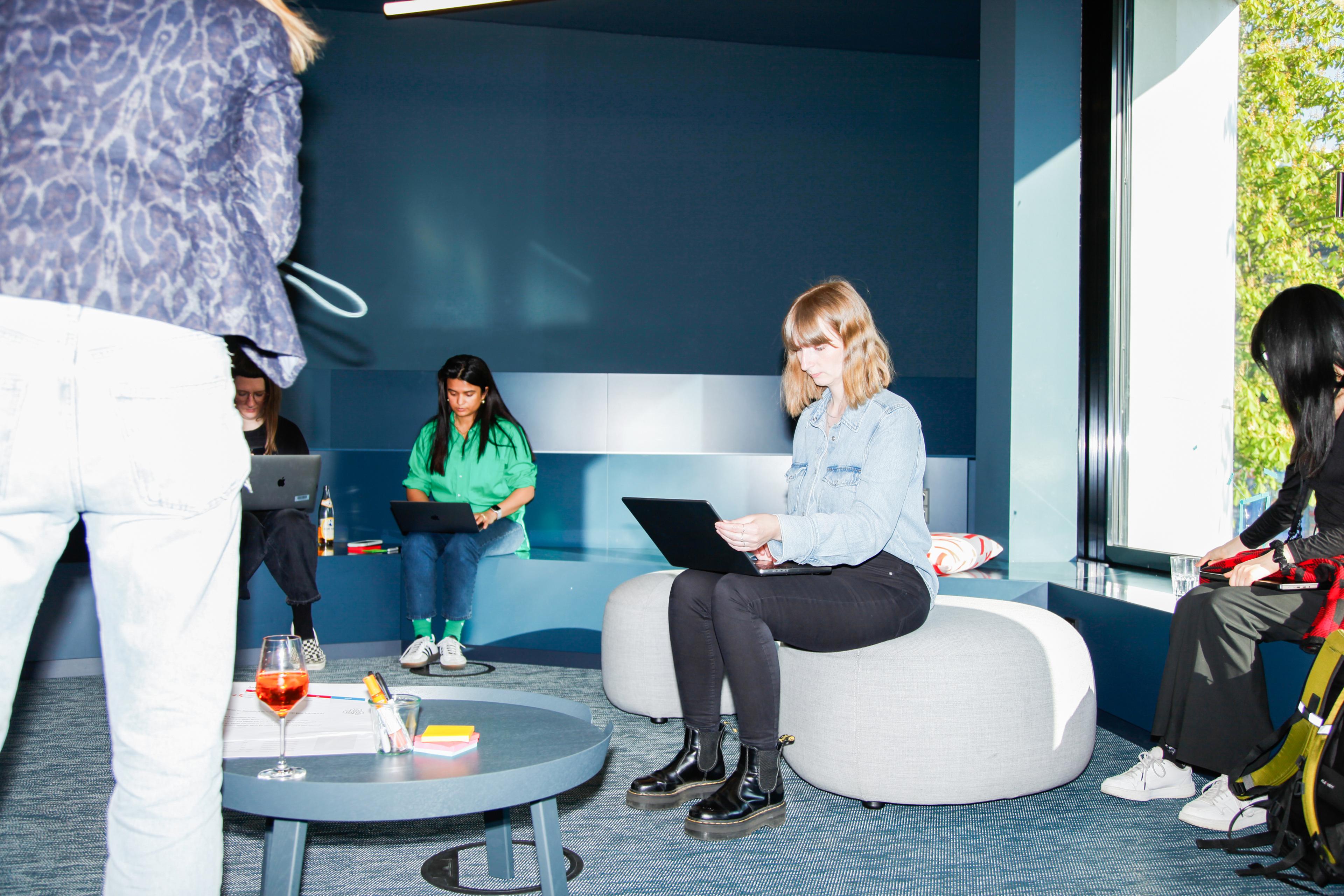 Four individuals seated in an open area, each using a computer.