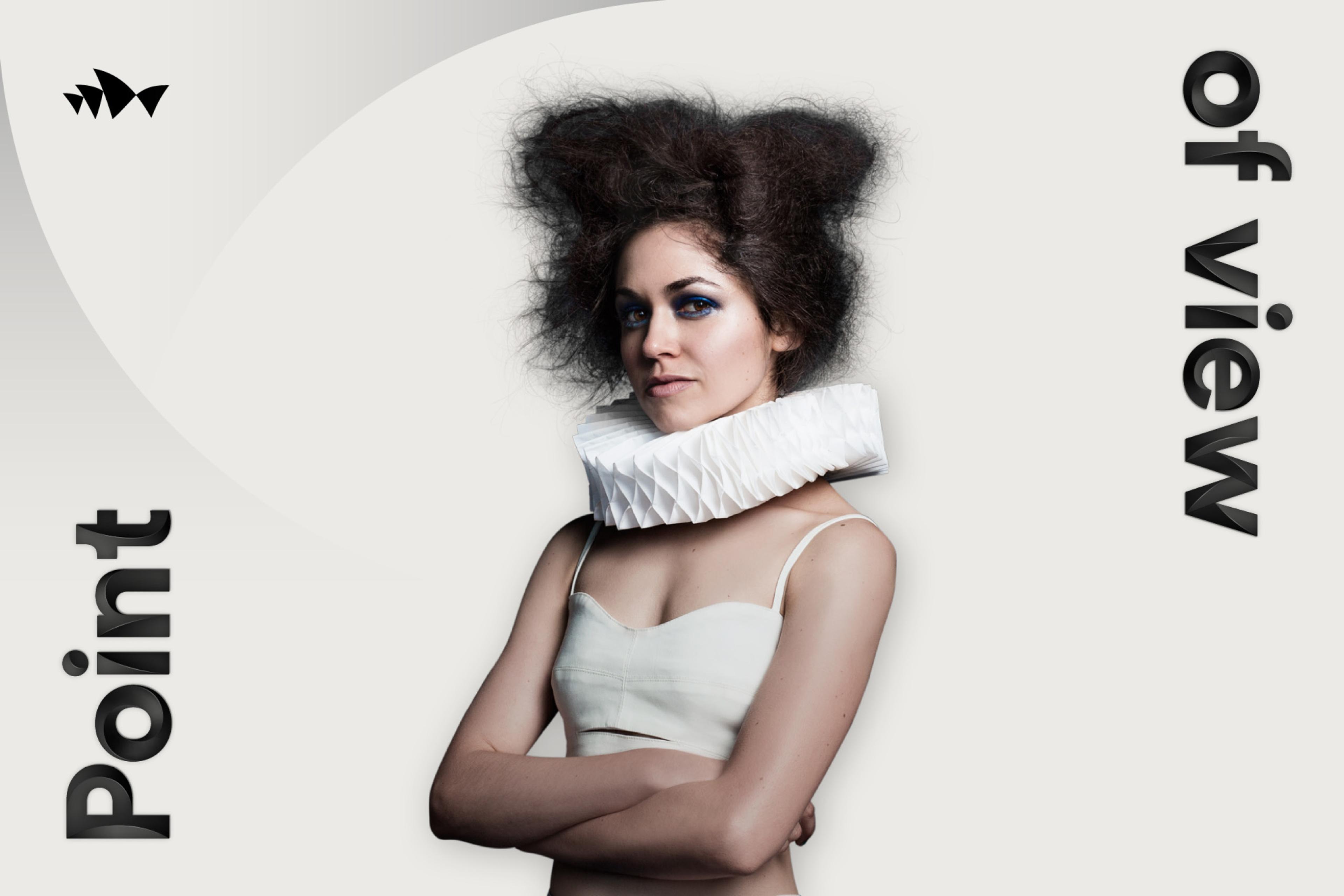 A female model gazes intently while wearing a white crop top and elaborate geometric paper ruff collar, augmented by vibrant blue eye makeup and voluminous dark hair. The phrase "Point of View" is positioned at either side of her.