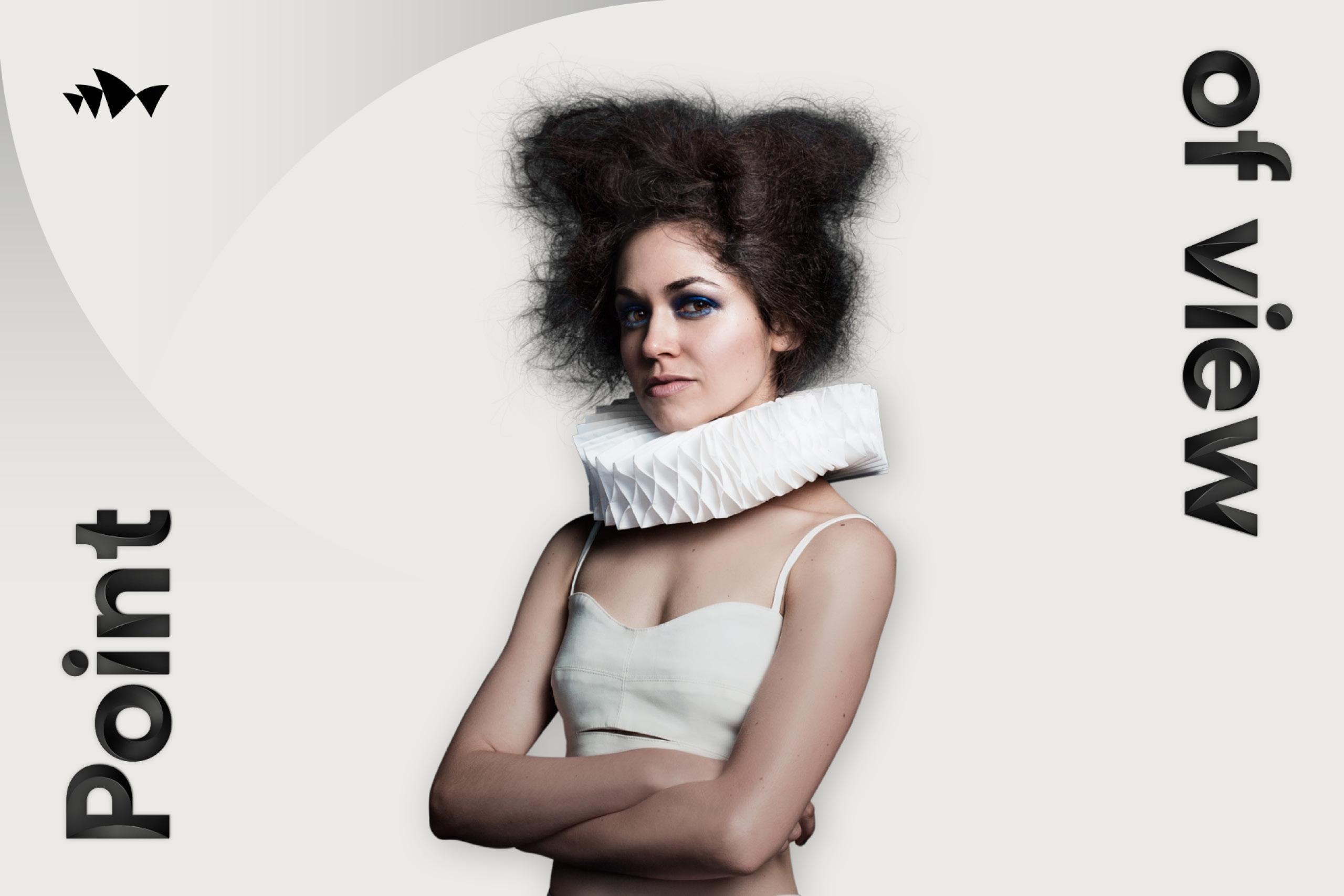 A female model gazes intently while wearing a white crop top and elaborate geometric paper ruff collar, augmented by vibrant blue eye makeup and voluminous dark hair. The phrase "Point of View" is positioned at either side of her.