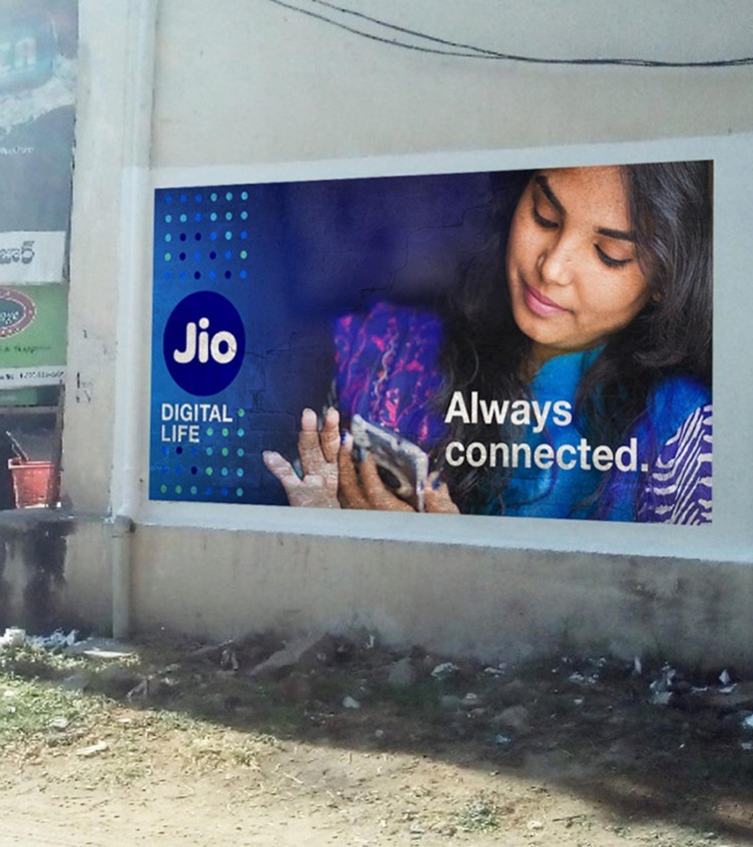 Outdoor advertisement for Jio Digital Life, featuring a woman with a gentle, downward gaze holding a cell phone, alongside the slogan "Always connected."