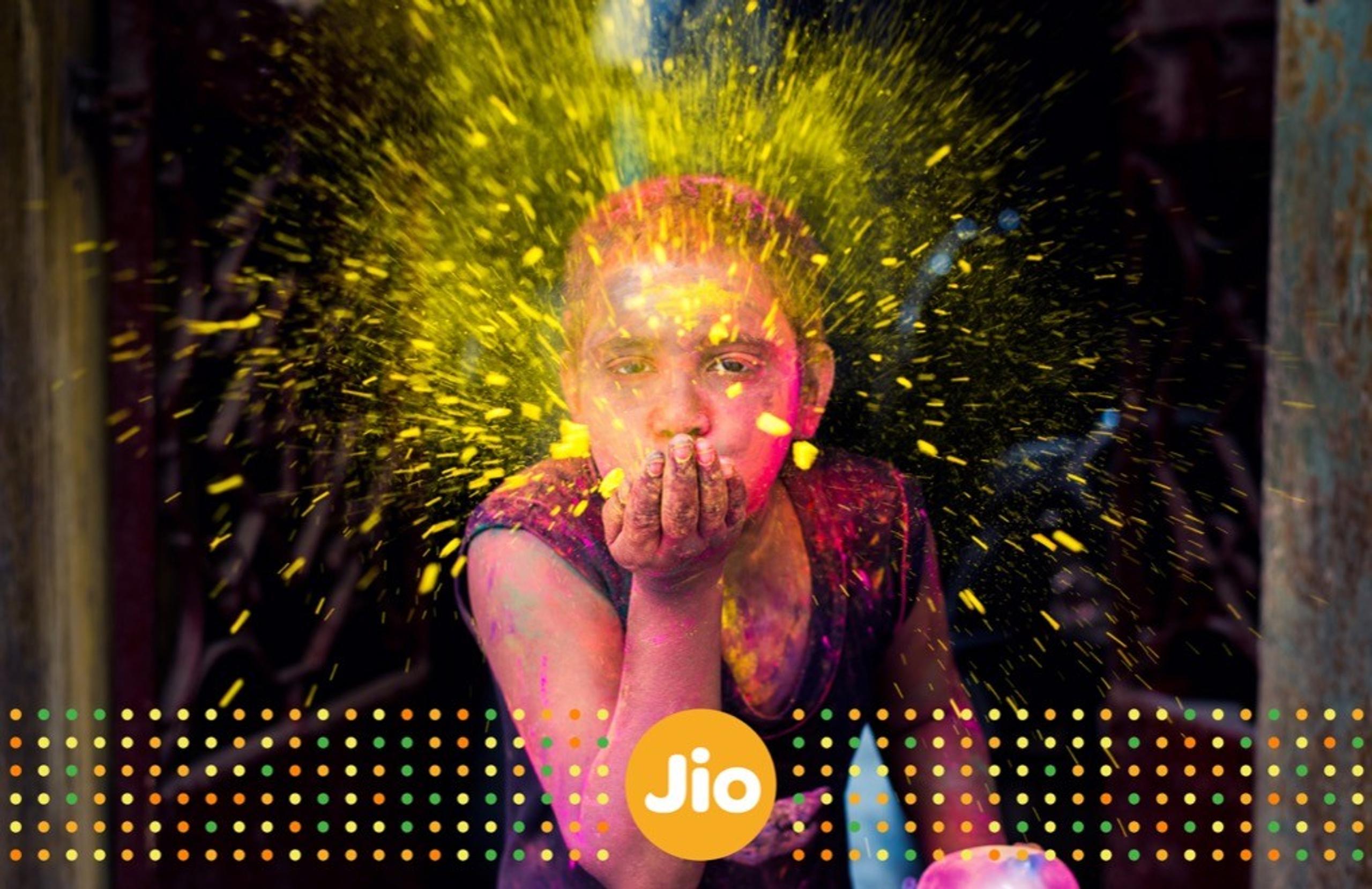 Girl, covered in colorful powder, blows a handful of yellow pigment towards the camera, representing festivity and celebration.