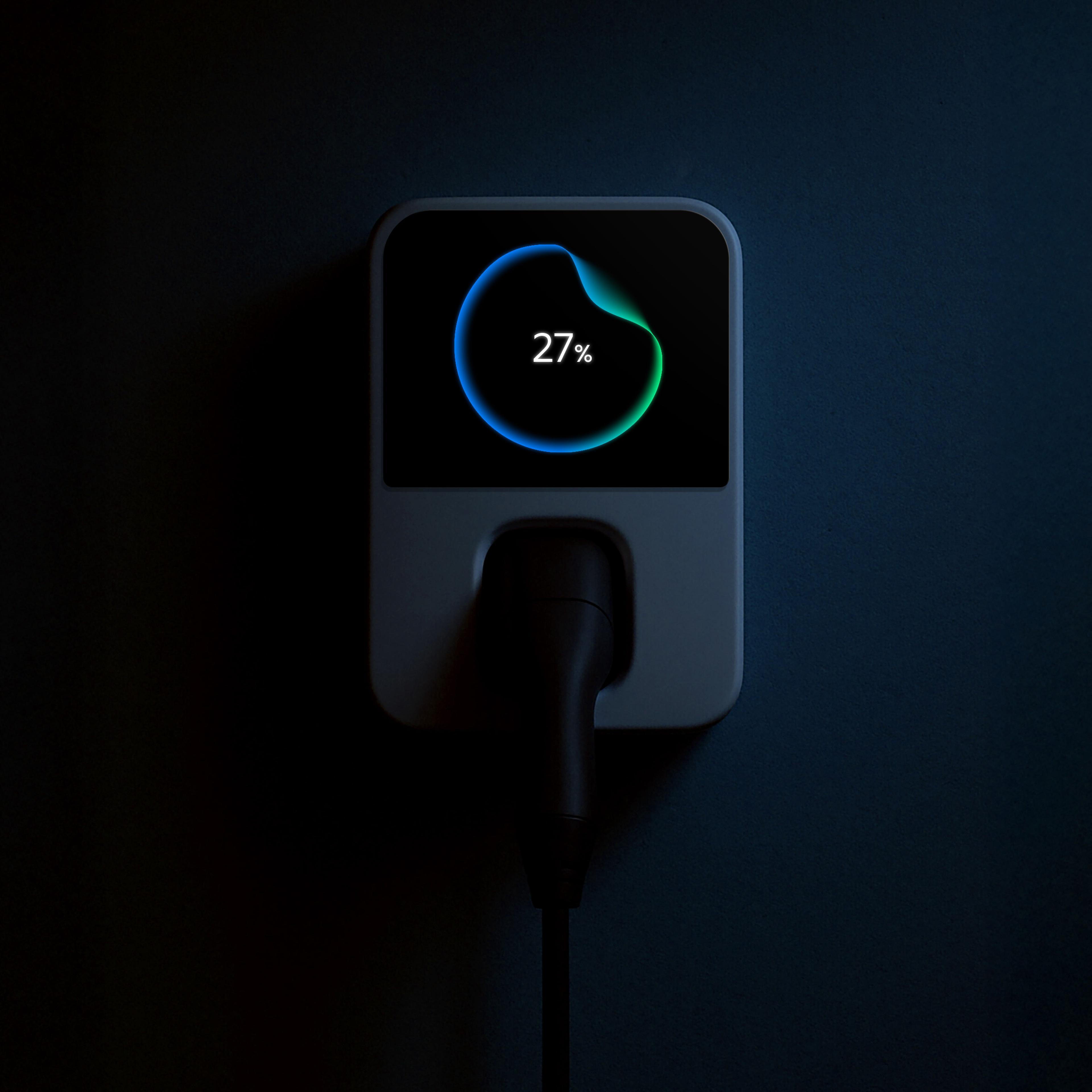 A charging device is mounted on a dark wall, displaying a circular progress bar with "27%" on its screen. A cable is plugged into the device.