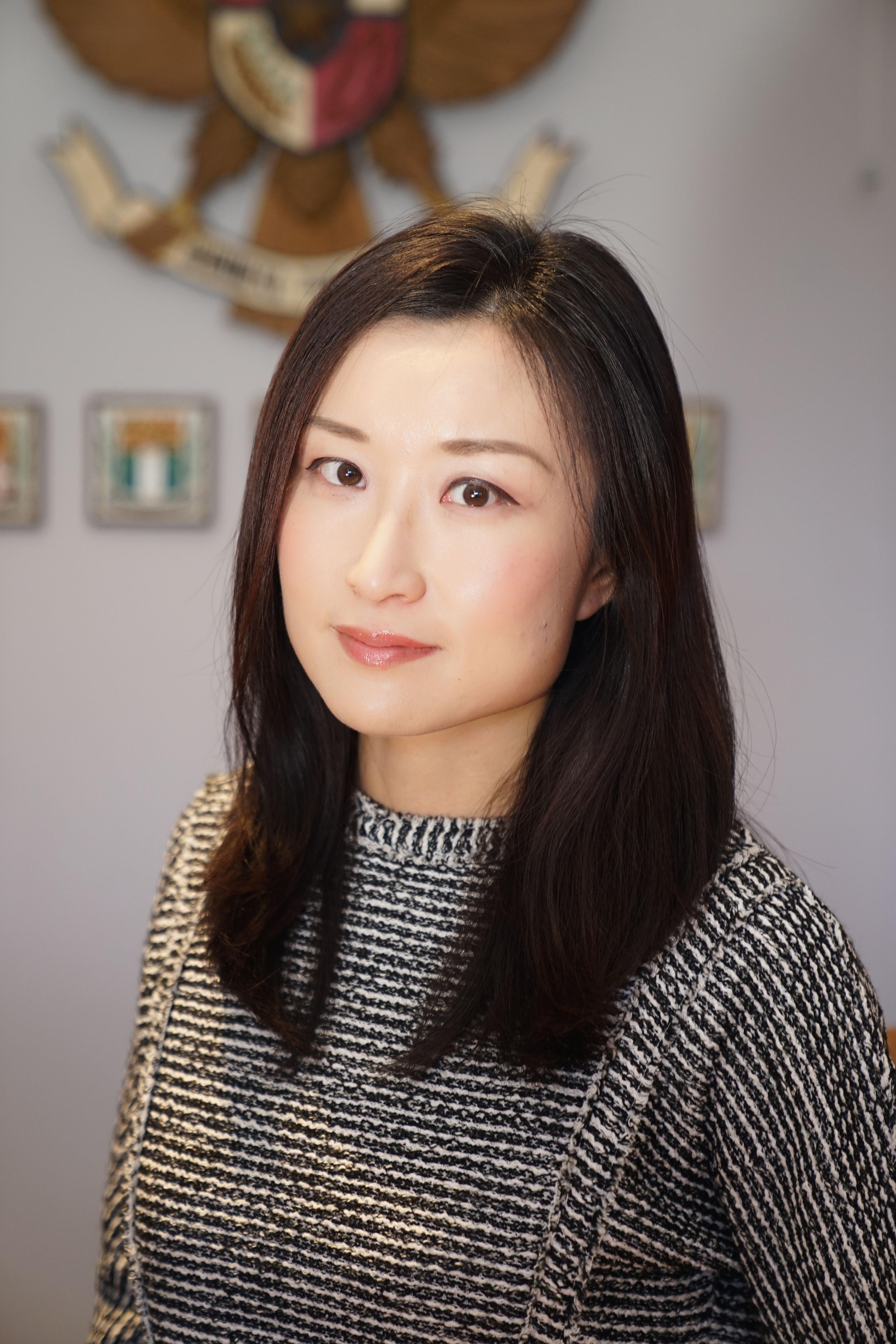 A woman poses. She has dark hair and wears a black and white patterned shirt.
